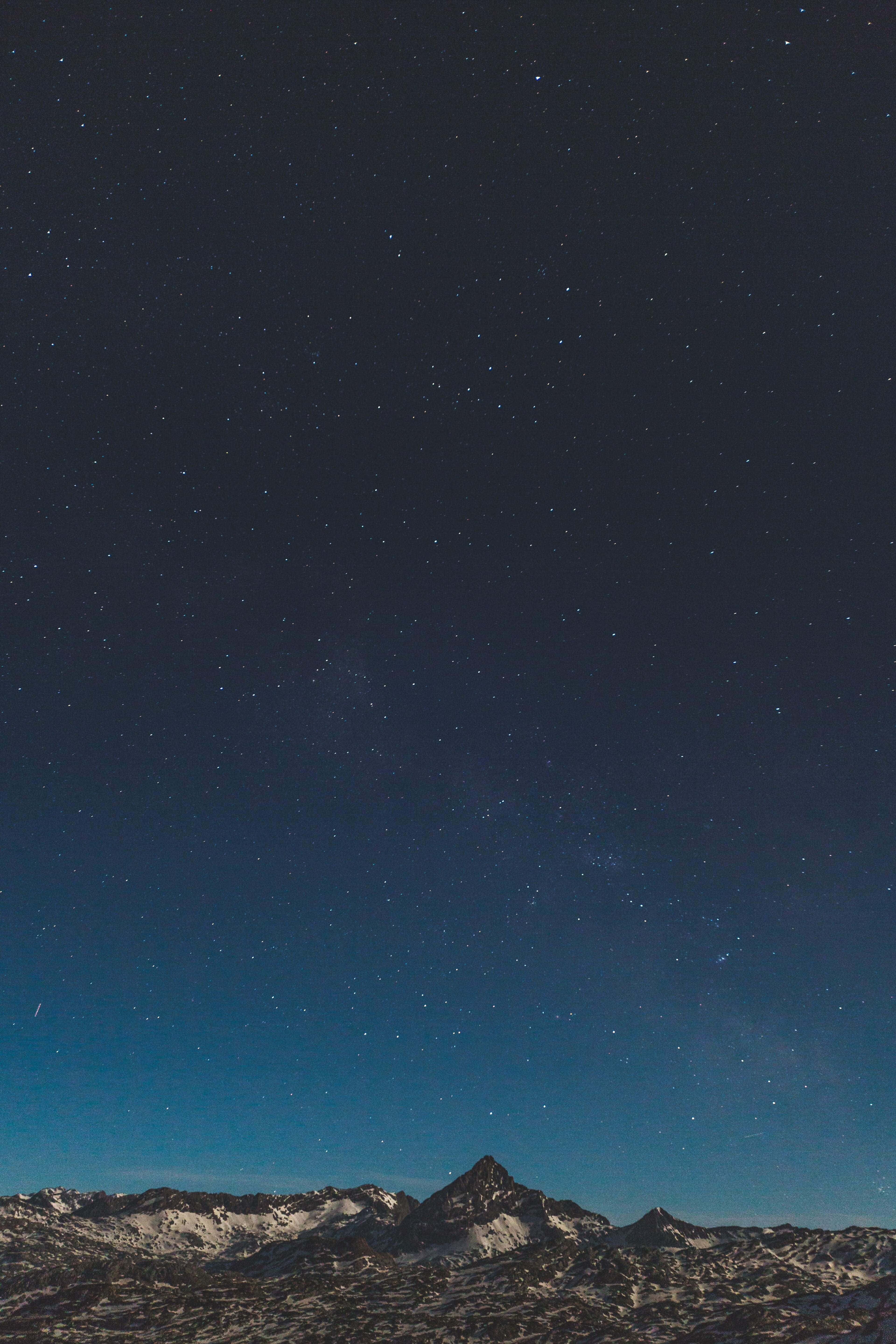 iPhone 桌布 壁紙 — 白雪覆蓋的山峰在廣闊的星空下聳立，星空閃爍著宇宙藍和深靛藍色調。