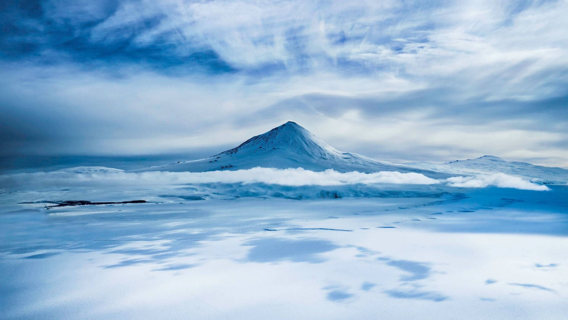 Antarctica 桌布 壁紙 — 白雪覆蓋的山峰在戲劇性的藍天下，從廣闊冰封景觀的雲海中升起。