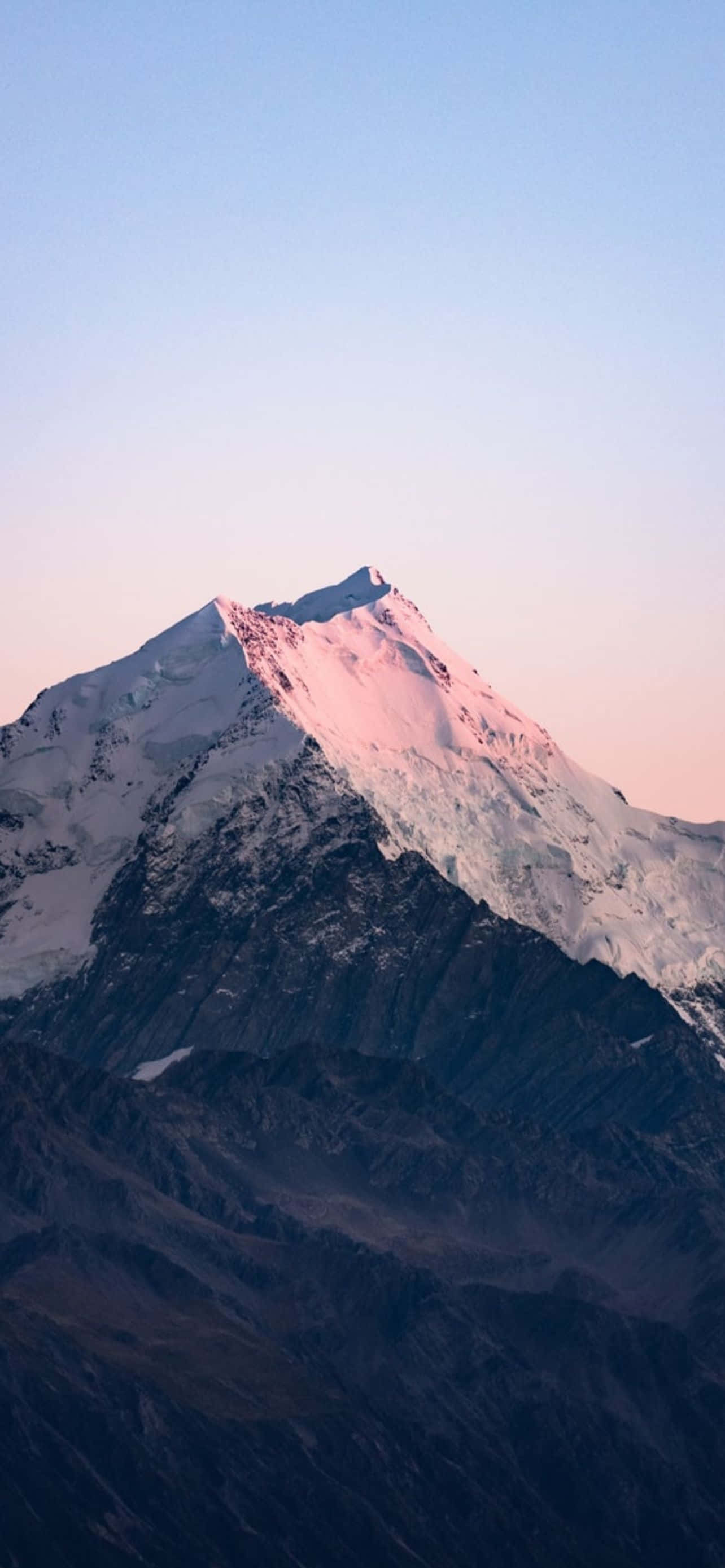 Mountain iPhone 桌布 壁紙 — 白雪覆蓋的山峰在日出時泛著粉紅色光芒，映襯著柔和的漸變天空。