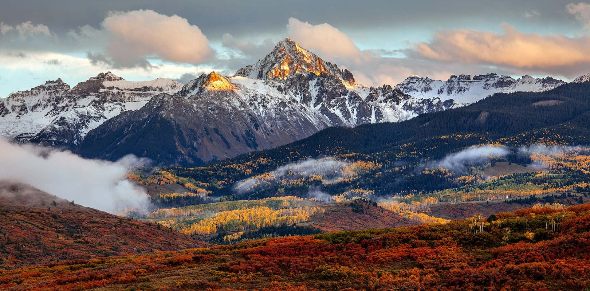 Colorado Mountain 桌布 壁紙 — 白雪覆蓋的山峰在日落時閃耀著金色光芒，下方是秋日紅黃交織、如火燃燒的森林。