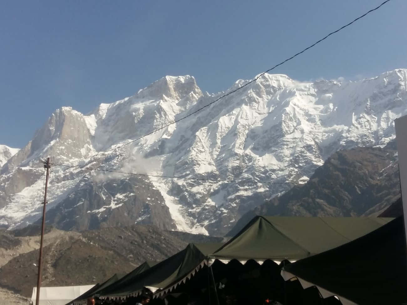 Kedarnath 桌布 壁紙 — 白雪覆蓋的山峰在晴朗的藍天下，在綠色帳篷後方雄偉地聳立。