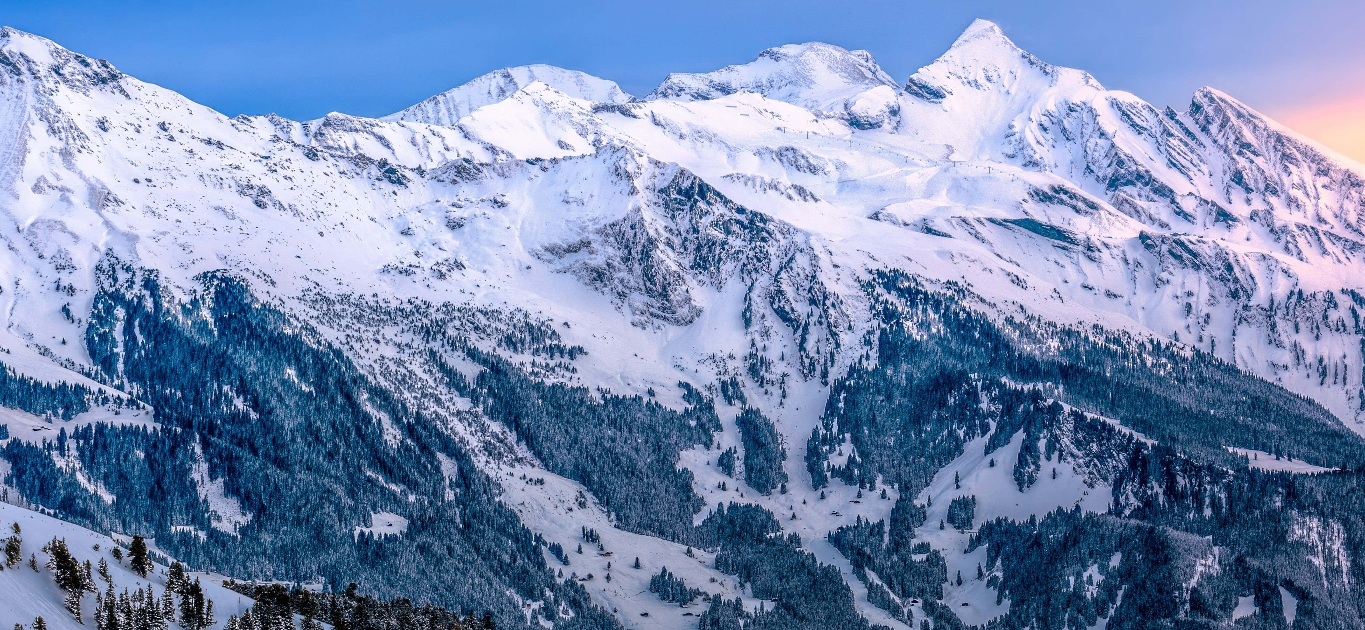 山景 桌布 壁紙 — 白雪覆蓋的山峰在暮色天空中雄偉地聳立，帶有柔和的粉紅色和藍色調。