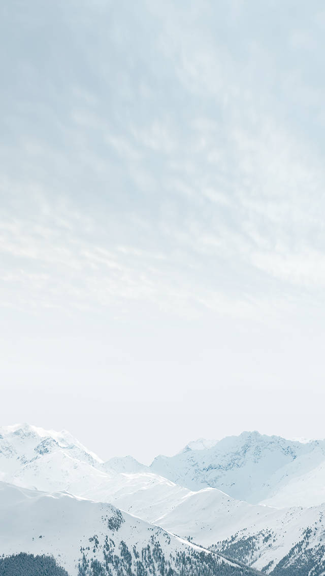 Winter 桌布 壁紙 — 白雪覆蓋的山峰在柔和淡藍色的天空下升起，伴隨著縷縷雲彩。