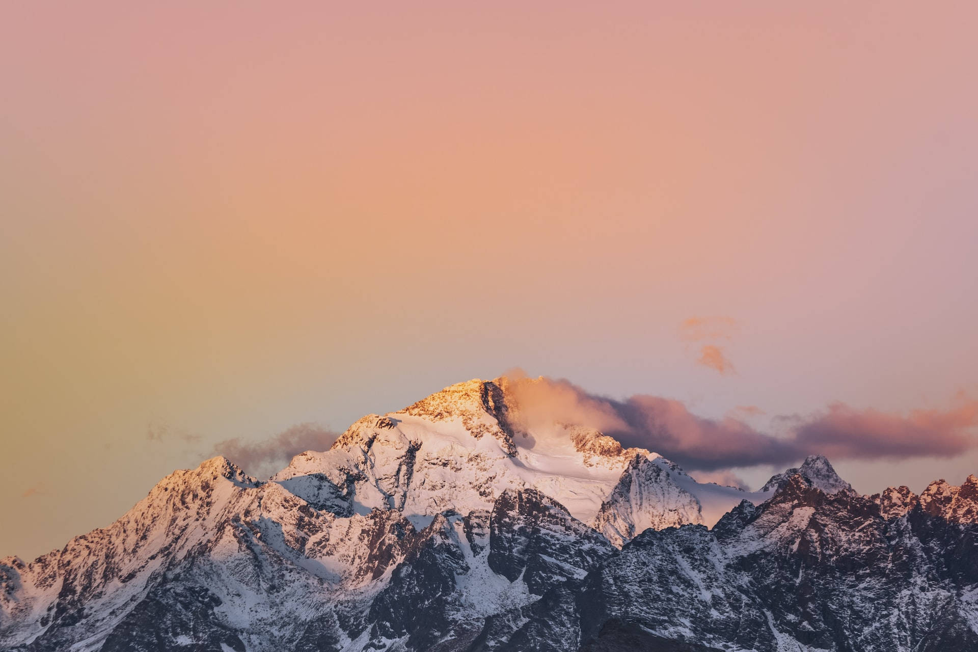Mountain Landscape 桌布 壁紙 — 白雪覆蓋的山峰在柔和的粉紅色和橙色天空映襯下，閃耀著溫暖的日落色調。