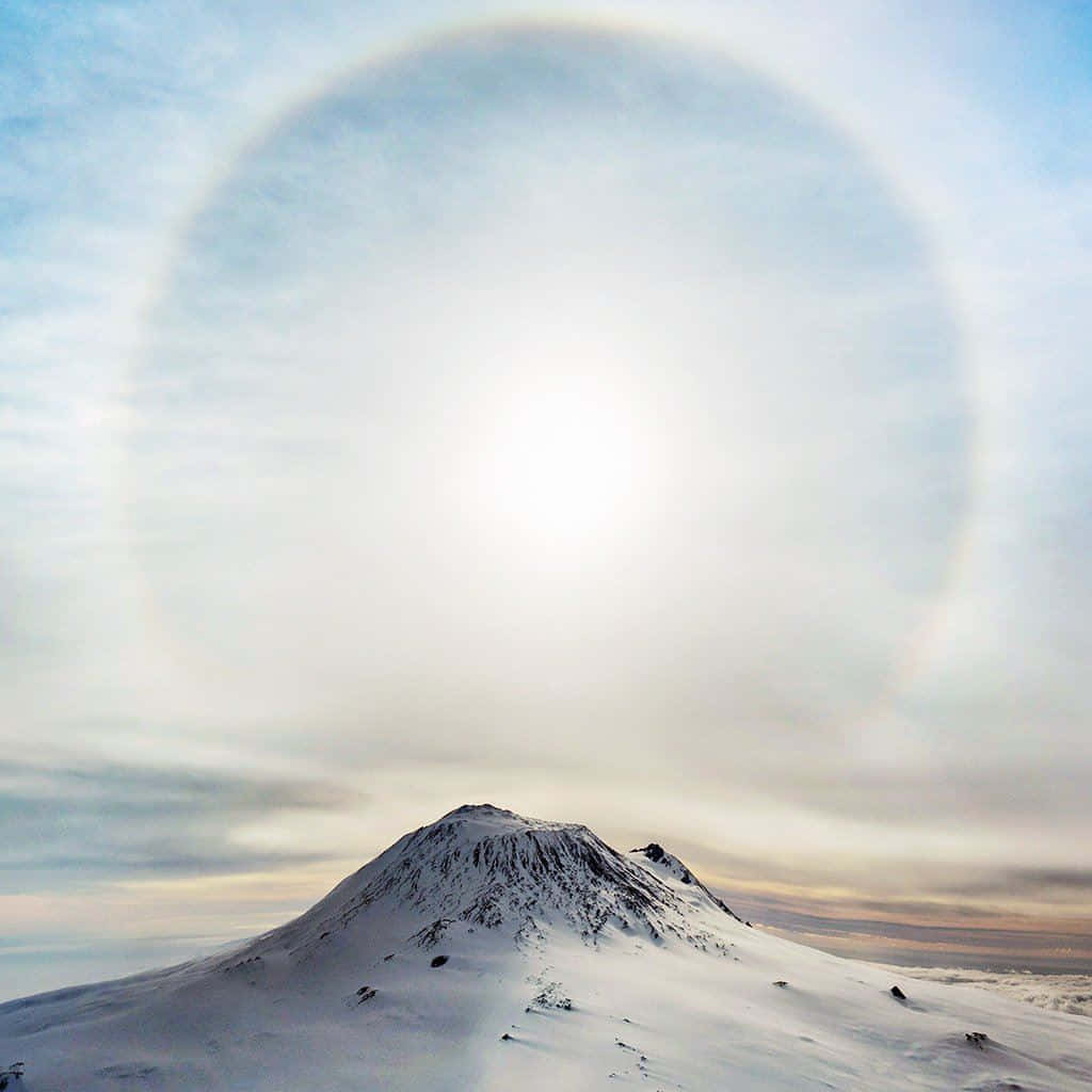 太陽 桌布 壁紙 — 白雪覆蓋的山峰在淡藍色天空中閃耀的太陽光環下升起。
