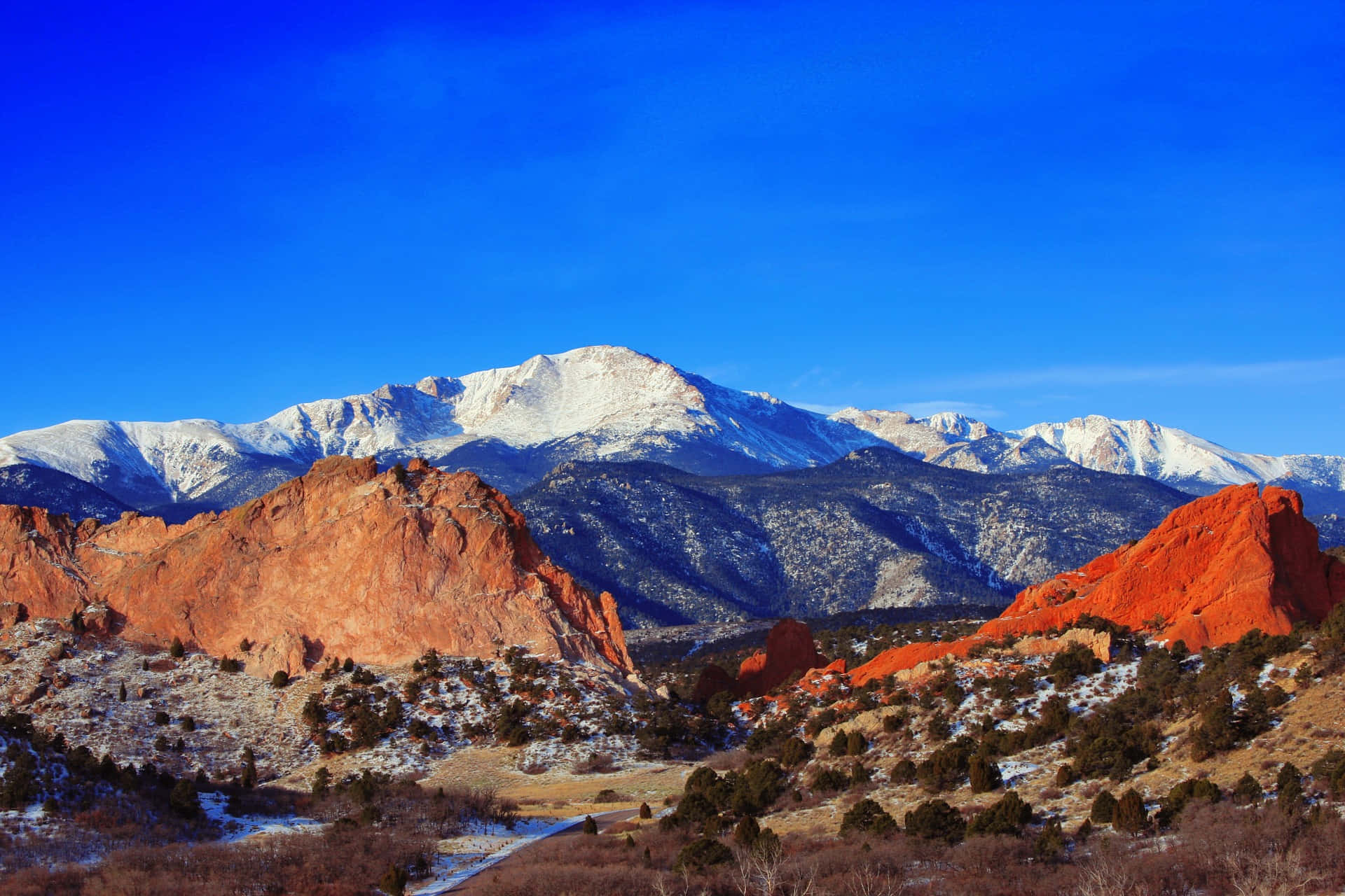 Colorado Mountain 桌布 壁紙 — 白雪覆蓋的山峰在清澈的藍天下，從鮮紅色的岩層後方升起。
