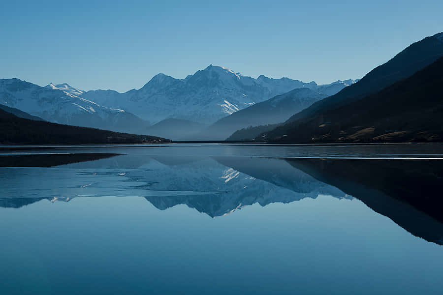 Cool Landscape 桌布 壁紙 — 白雪覆蓋的山峰在清澈的藍天下，雄偉地聳立在玻璃般的湖泊後方，湖面倒映著山巔。