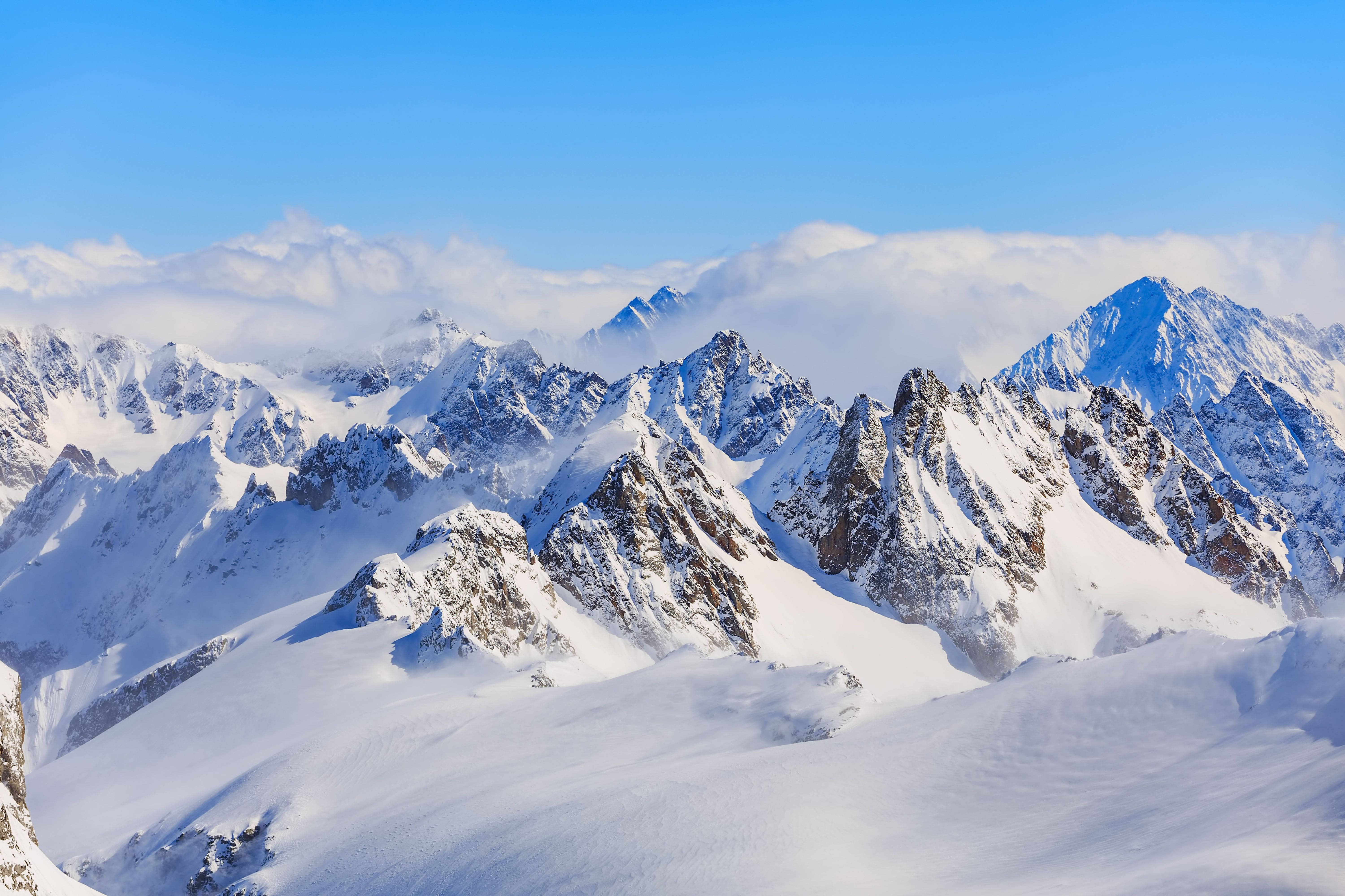 自然 4K 桌布 壁紙 — 白雪覆蓋的山峰在清澈藍天下穿透雲層，呈現令人驚嘆的阿爾卑斯山景。