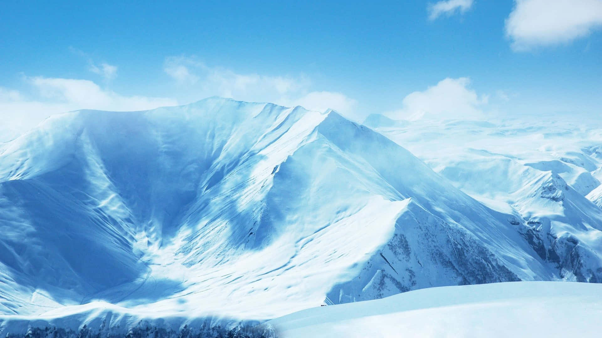 Snowy Mountain 桌布 壁紙 — 白雪覆蓋的山峰在清澈藍天和縷縷白雲下巍然聳立。