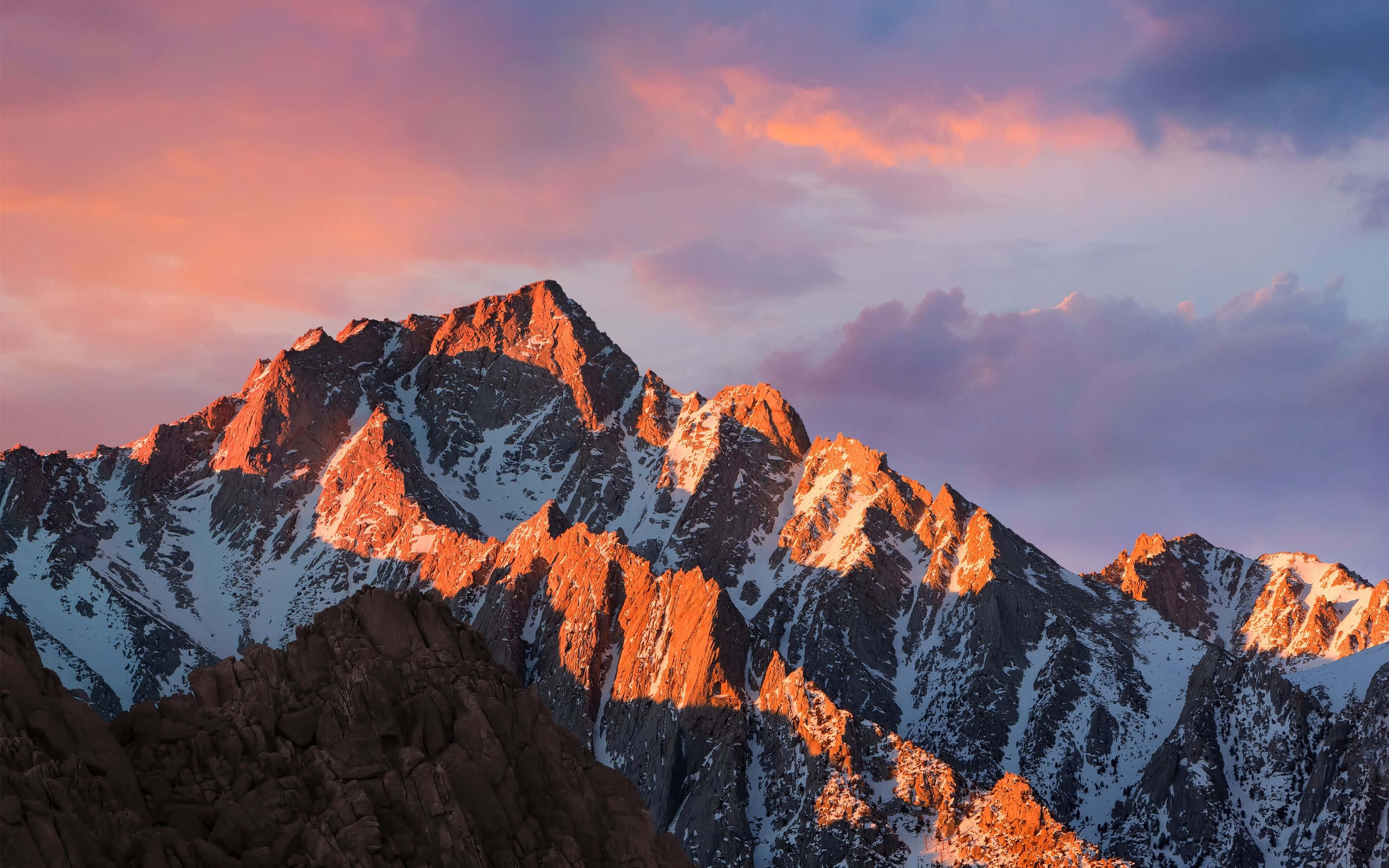 macbook pro aesthetic 桌布 壁紙 — 白雪覆蓋的山峰在溫暖的夕陽光下閃耀，映襯著充滿活力的粉紅色和紫色天空。