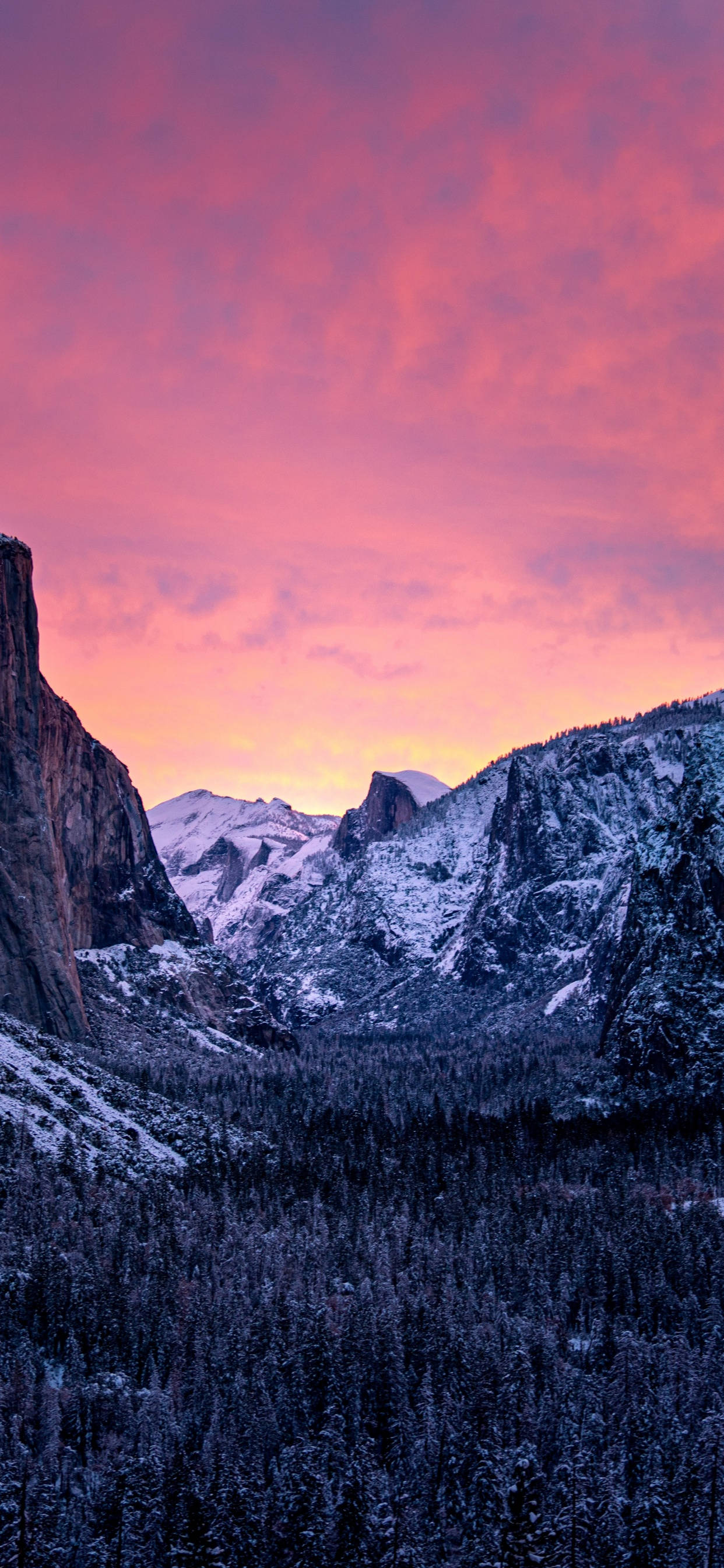 Yosemite iPhone 桌布 壁紙 — 白雪覆蓋的山峰在火紅的粉紅和橙色日落天空下，聳立在森林覆蓋的山谷之上。