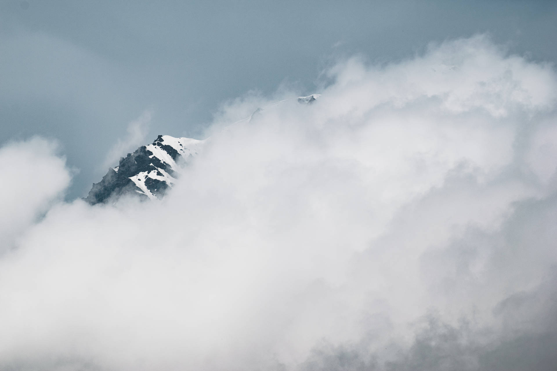 白雪覆蓋的山峰在陰沉天空下聳立於厚厚雲層之上。