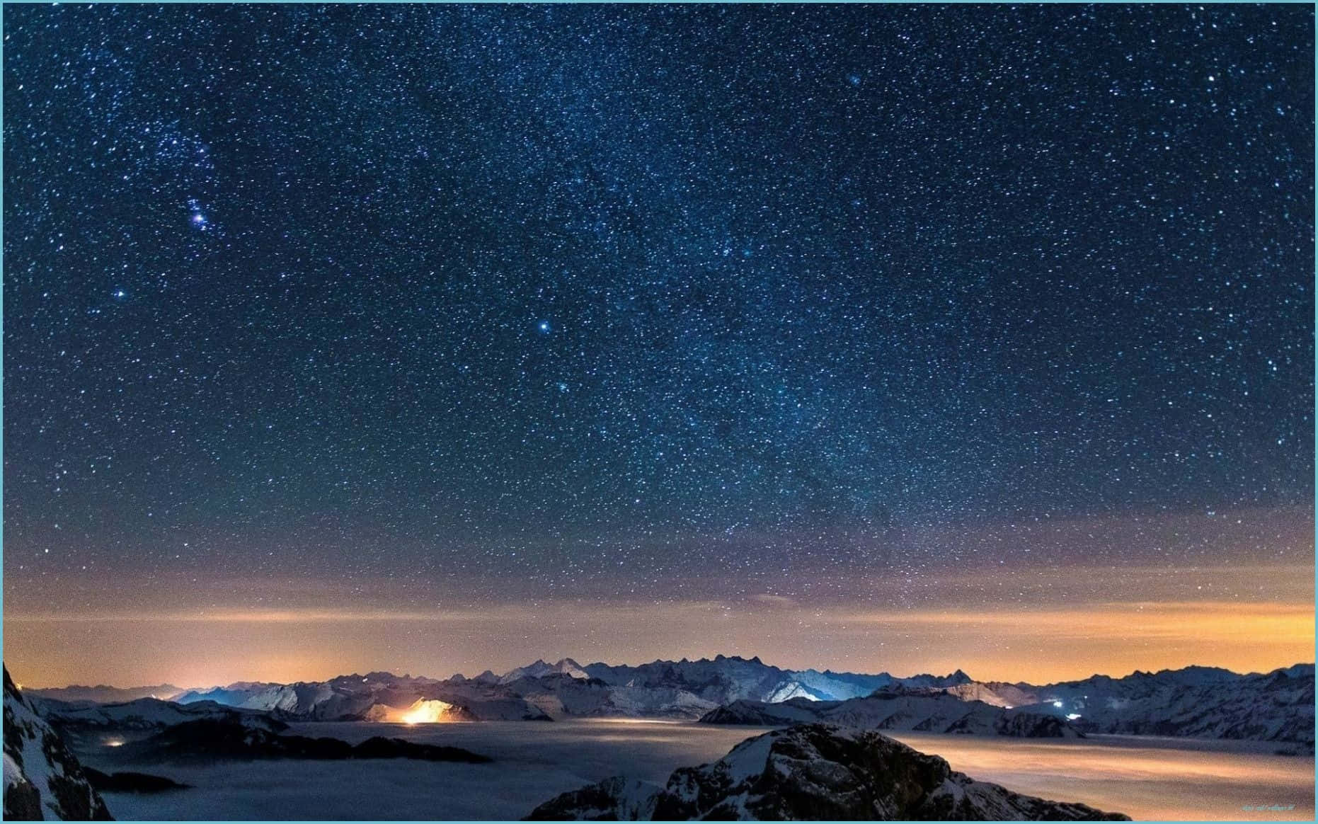 桌布 壁紙 — 白雪覆蓋的山峰在繁星點點的夜空下升起，夜空閃爍著極光和遠處的光芒。