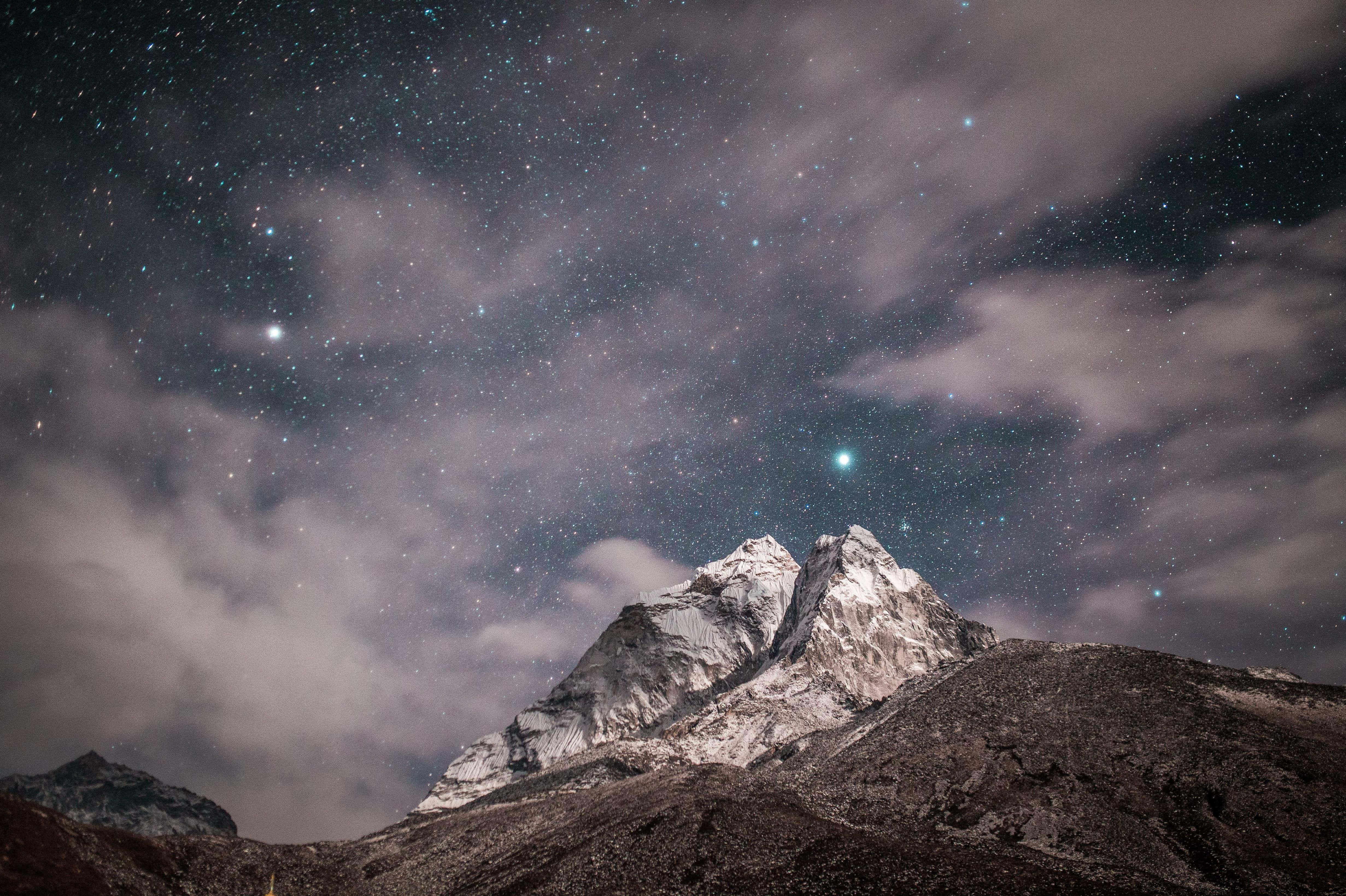 Himalaya 桌布 壁紙 — 白雪覆蓋的山峰在繁星點點的夜空下聳立，有飄動的雲朵和一顆可見的彗星。