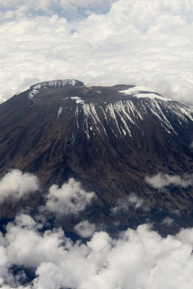 Tanzania 桌布 壁紙 — 白雪覆蓋的山峰在蓬鬆的白雲之上聳立，帶有崎嶇的棕色山坡的航拍視圖。