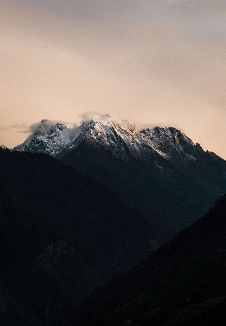 高清 桌布 壁紙 — 白雪覆蓋的山峰在黃昏時分柔和地發光，雲朵飄過其崎嶇的山脊。