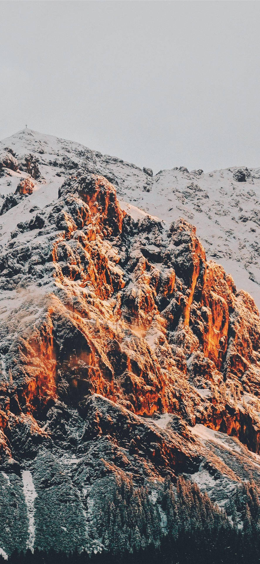  壁紙 — 白雪覆蓋的山峰沐浴在溫暖的金色光芒中，映襯著蒼白的天空。