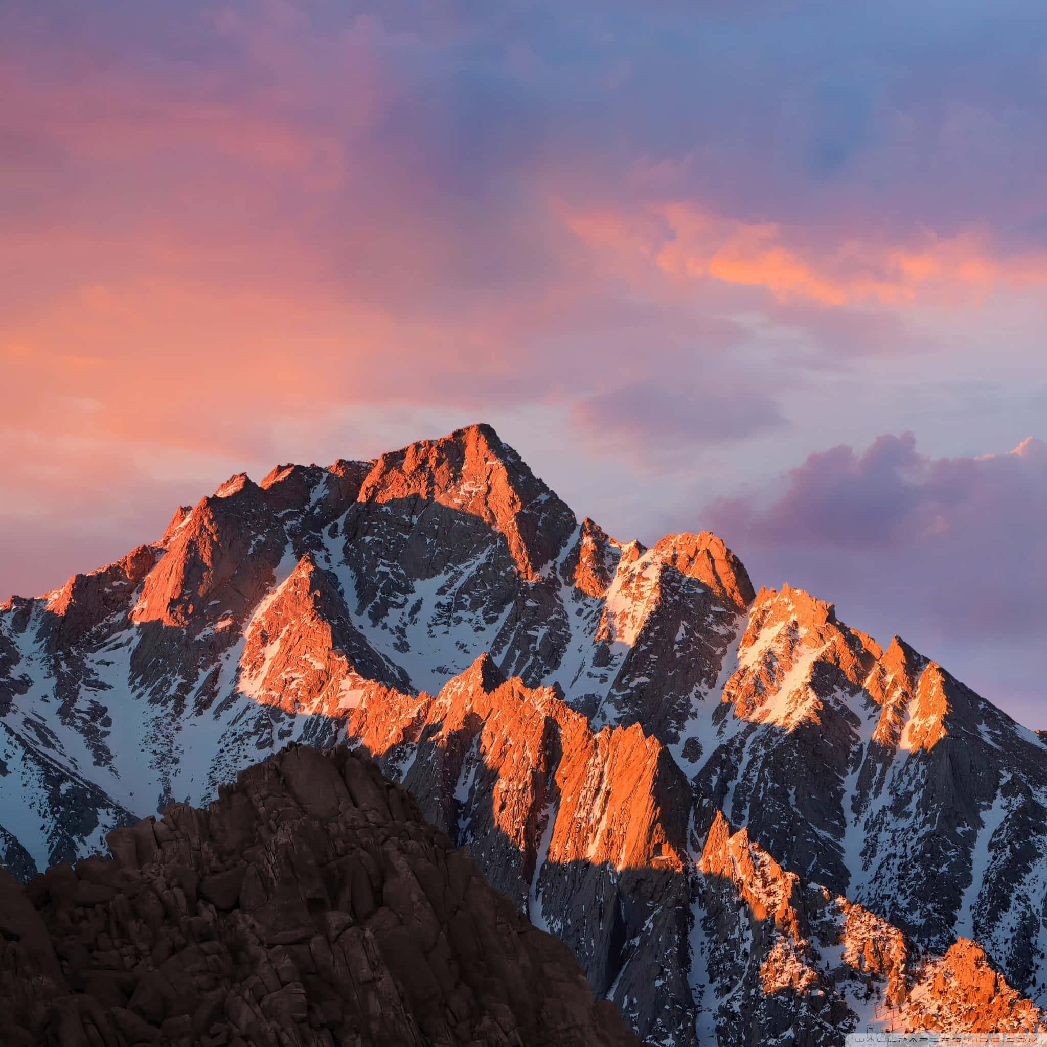iPad 2 桌布 壁紙 — 白雪覆蓋的山峰沐浴在金色的日落光芒中，映襯著充滿活力的粉紅色和紫色天空。