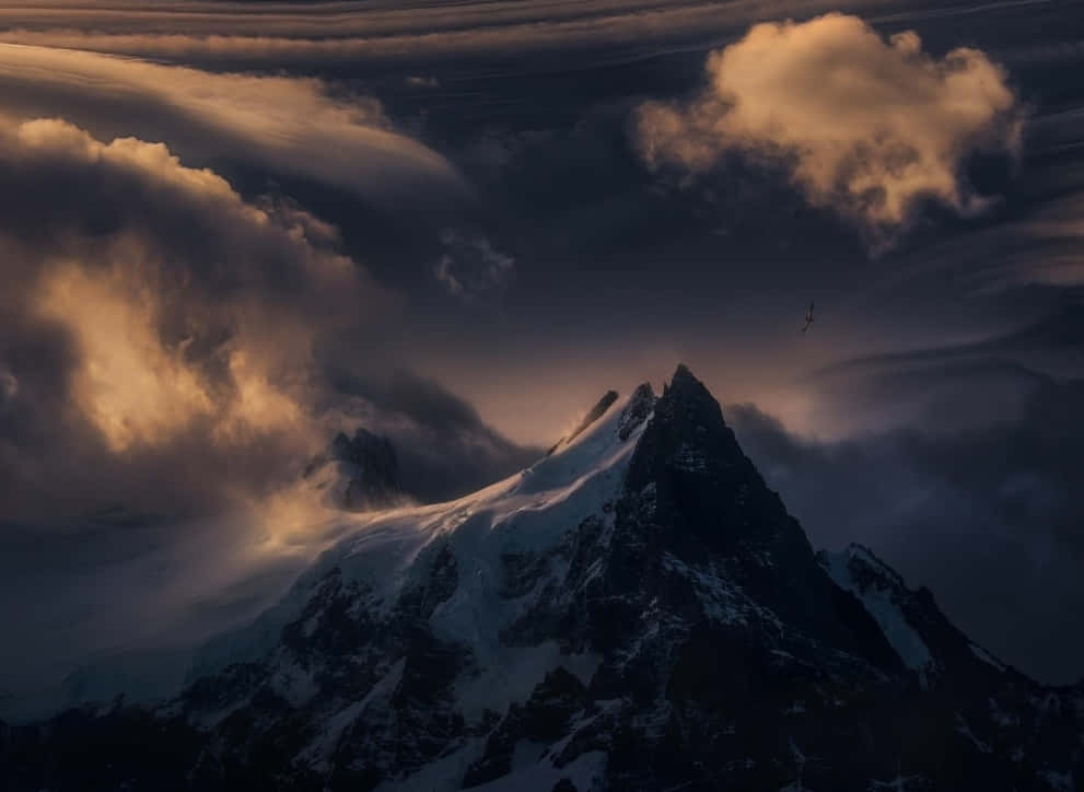 Patagonia 桌布 壁紙 — 白雪覆蓋的山峰穿破沐浴在金色日落光芒中的戲劇性雲層。