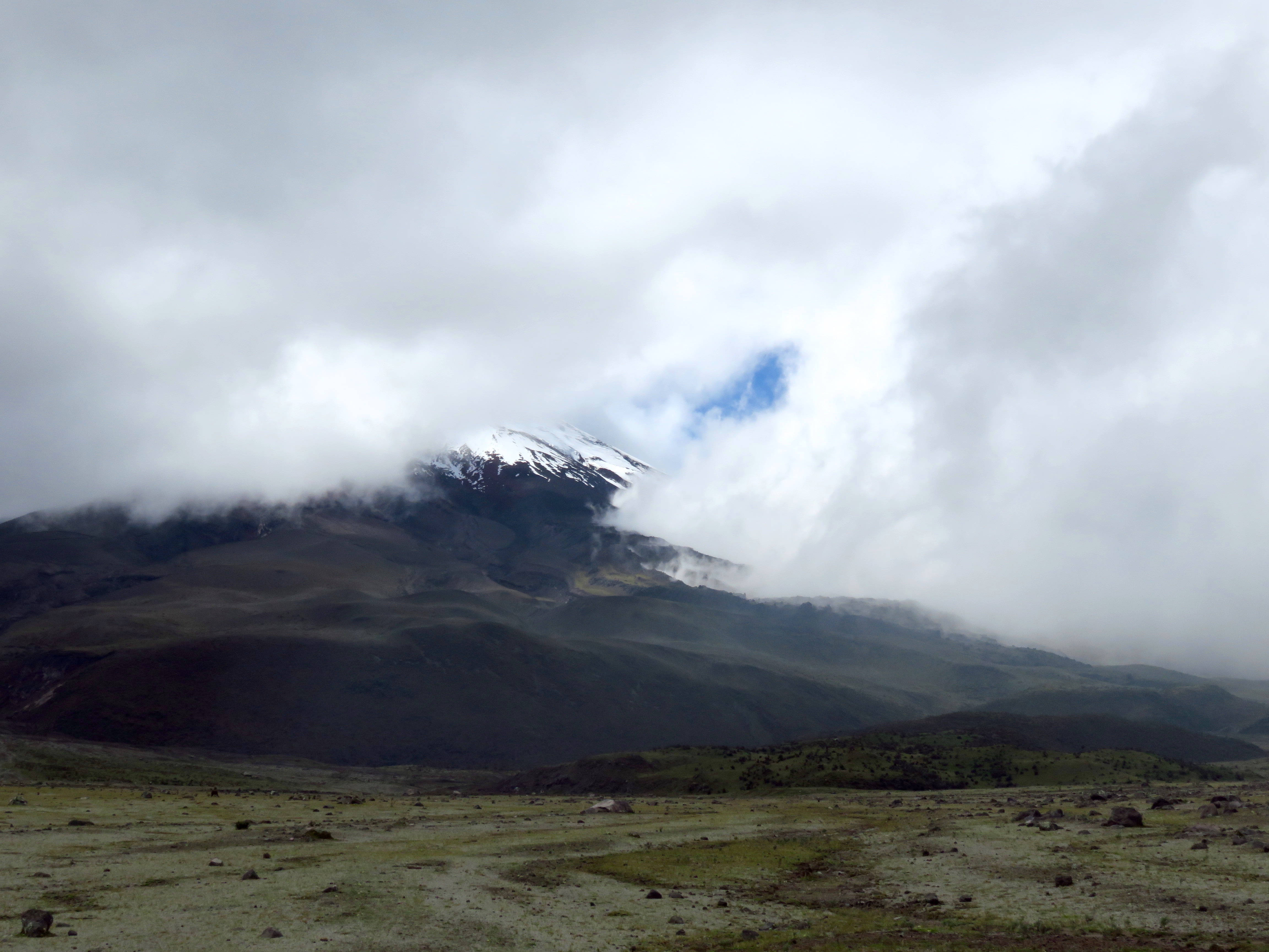 Ecuador 桌布 壁紙 — 白雪覆蓋的山峰穿透厚雲，出現在廣闊的綠色和棕色谷底之上。