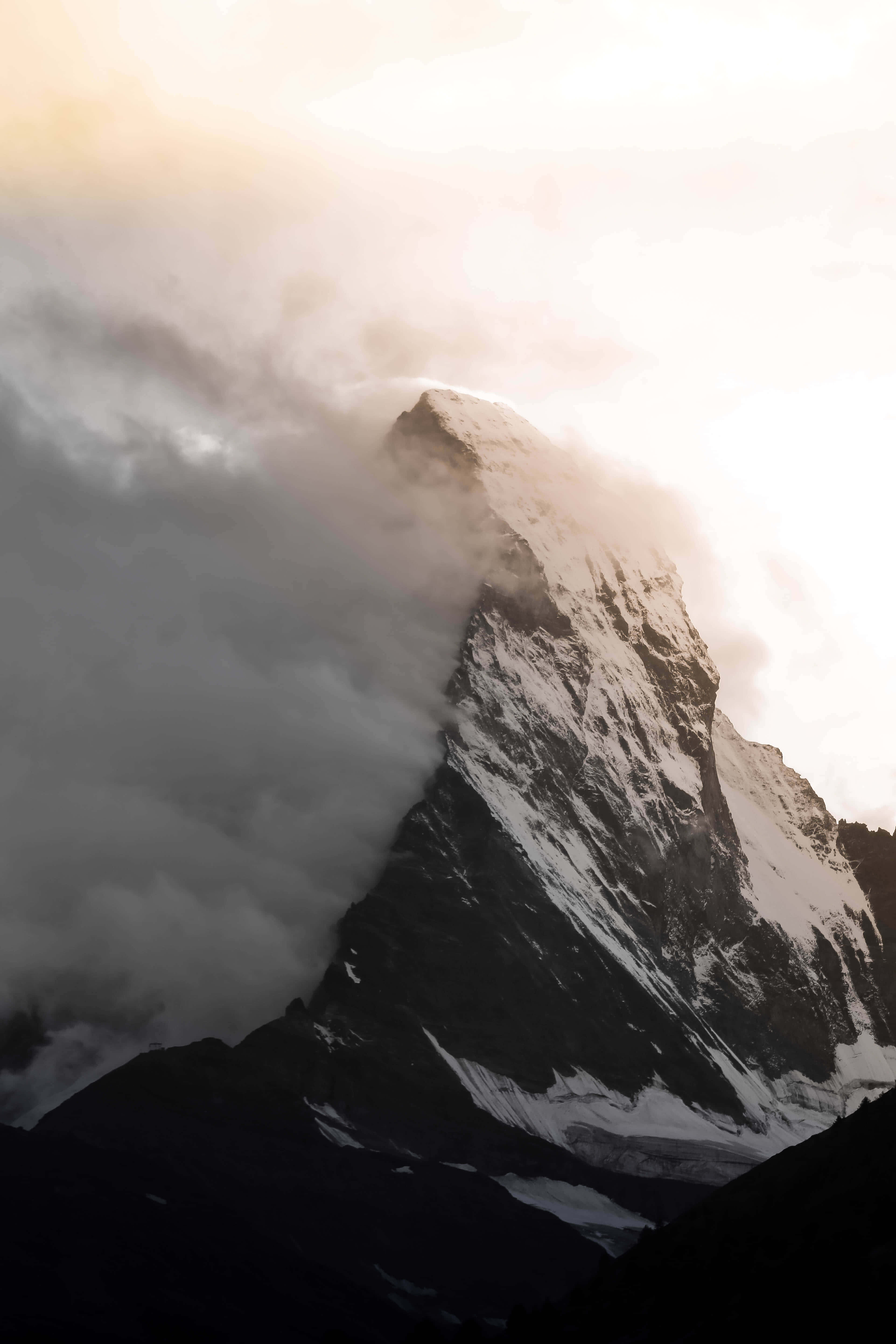 桌布 壁紙 — 白雪覆蓋的山峰穿過戲劇性的雲層，金色陽光從上方穿透而出。