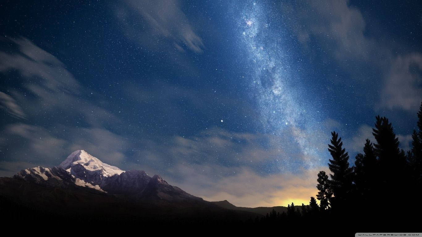Starry 桌布 壁紙 — 白雪覆蓋的山峰聳立在充滿活力的星空下，銀河拱橋般橫跨天際。