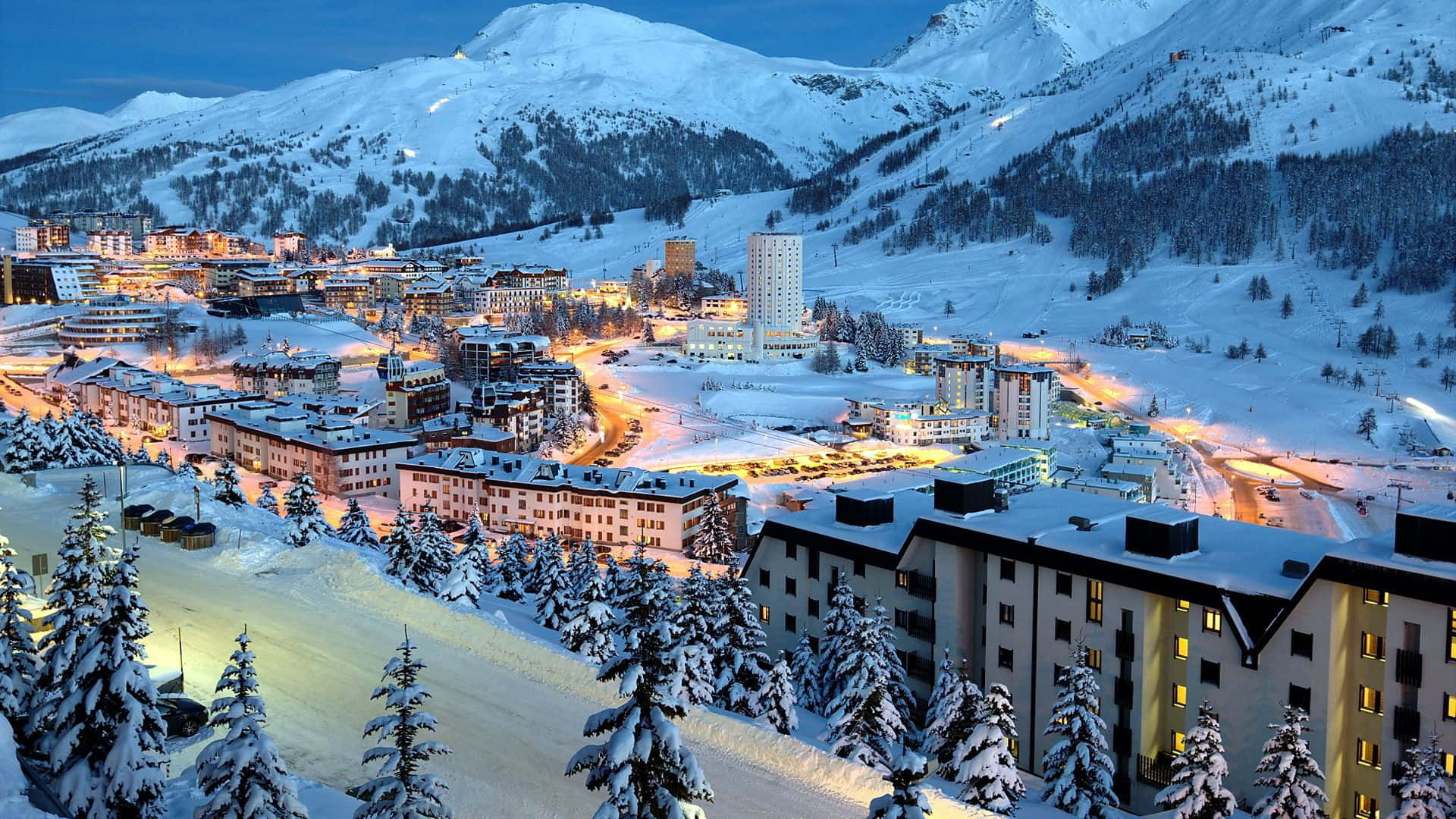 Ski Resort 桌布 壁紙 — 白雪覆蓋的山村在深藍色的暮色天空中閃爍著溫暖的燈光。