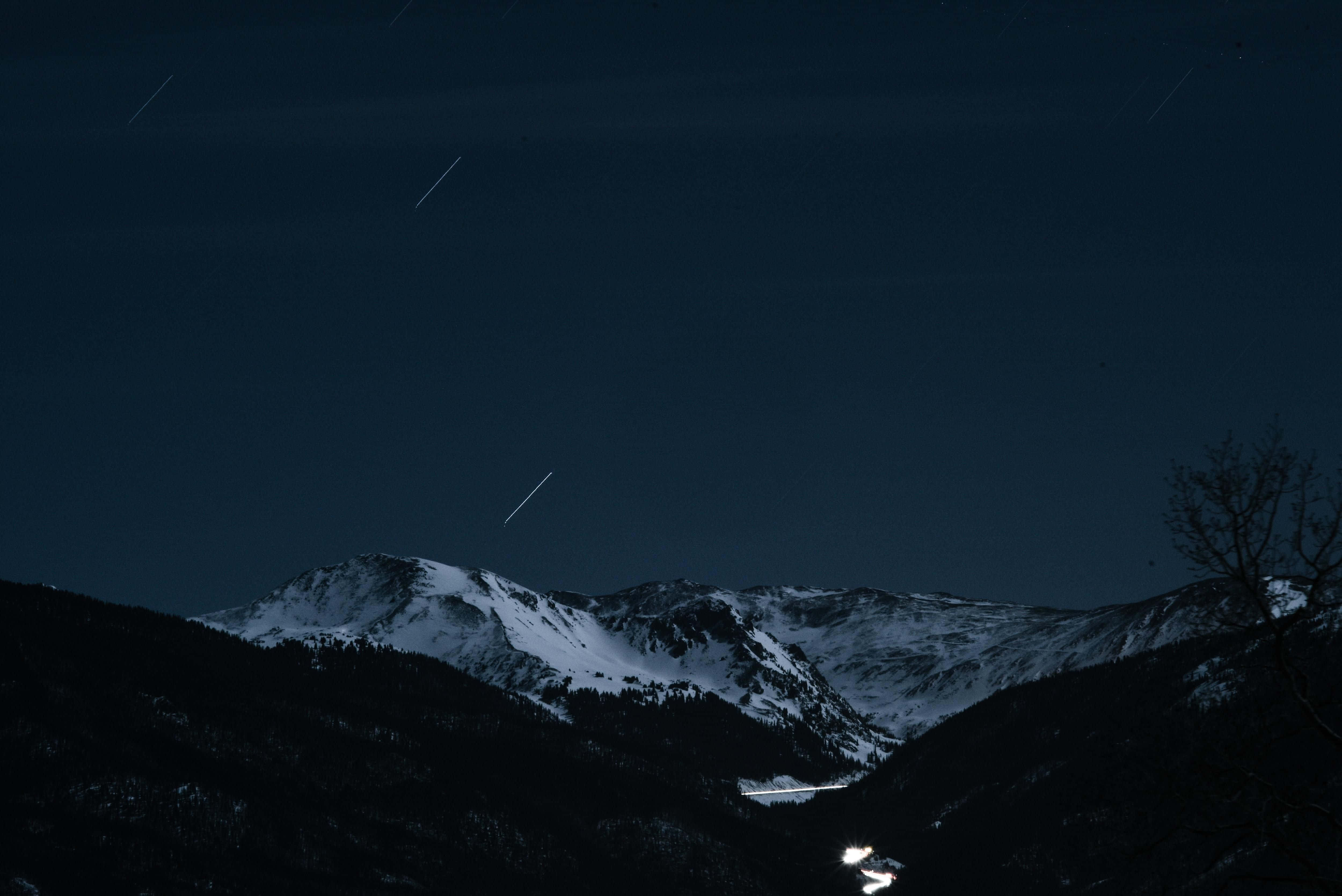 Dark Landscape 桌布 壁紙 — 白雪覆蓋的山脈，在繁星點點的夜空下，可見星軌和遠處發光的山谷。