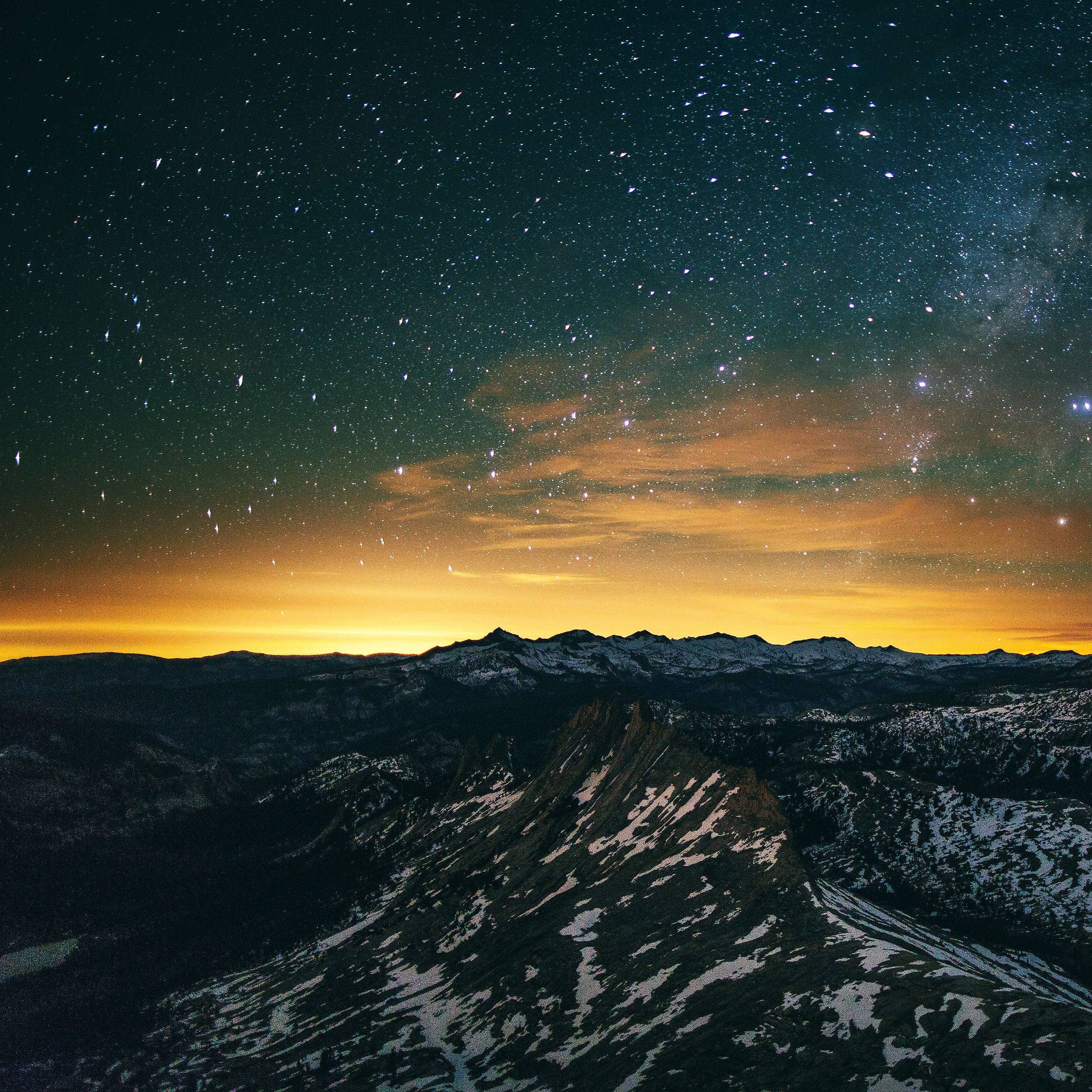 iPad Pro 桌布 壁紙 — 白雪覆蓋的山脈在繁星點點的夜空下升起，夜空閃爍著橙色極光雲。
