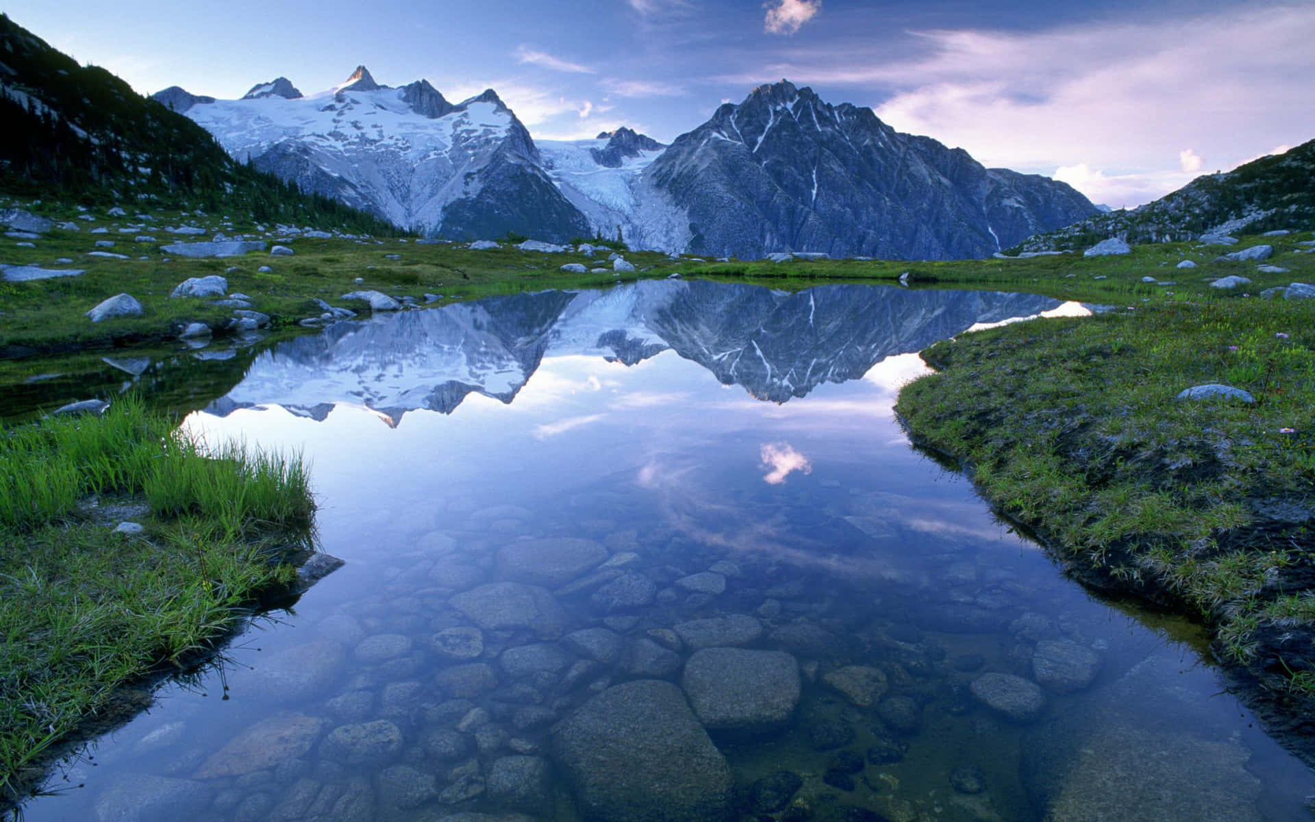 山景 桌布 壁紙 — 白雪覆蓋的山脈在黃昏時分完美地倒映在一個被綠草和岩石環繞的寧靜高山湖泊中。