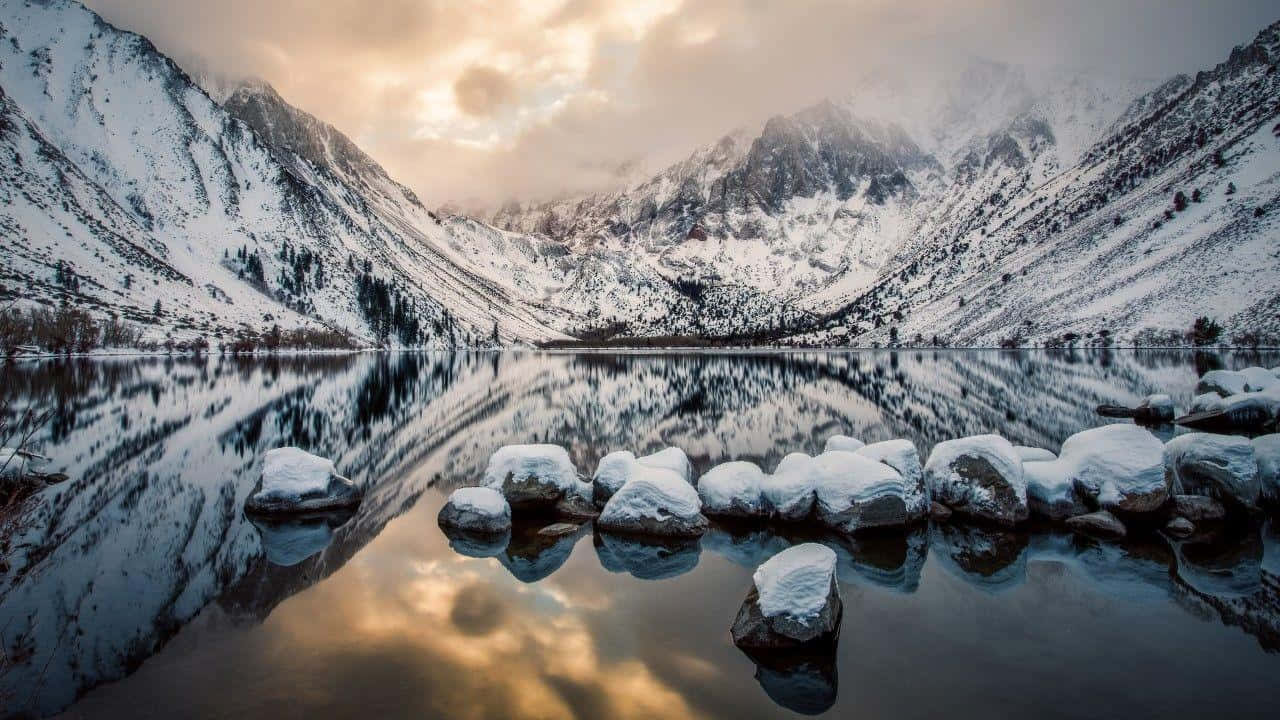 加州 桌布 壁紙 — 白雪覆蓋的山脈完美地倒映在平靜的湖面上，金色的夕陽光芒穿過雲層閃耀。