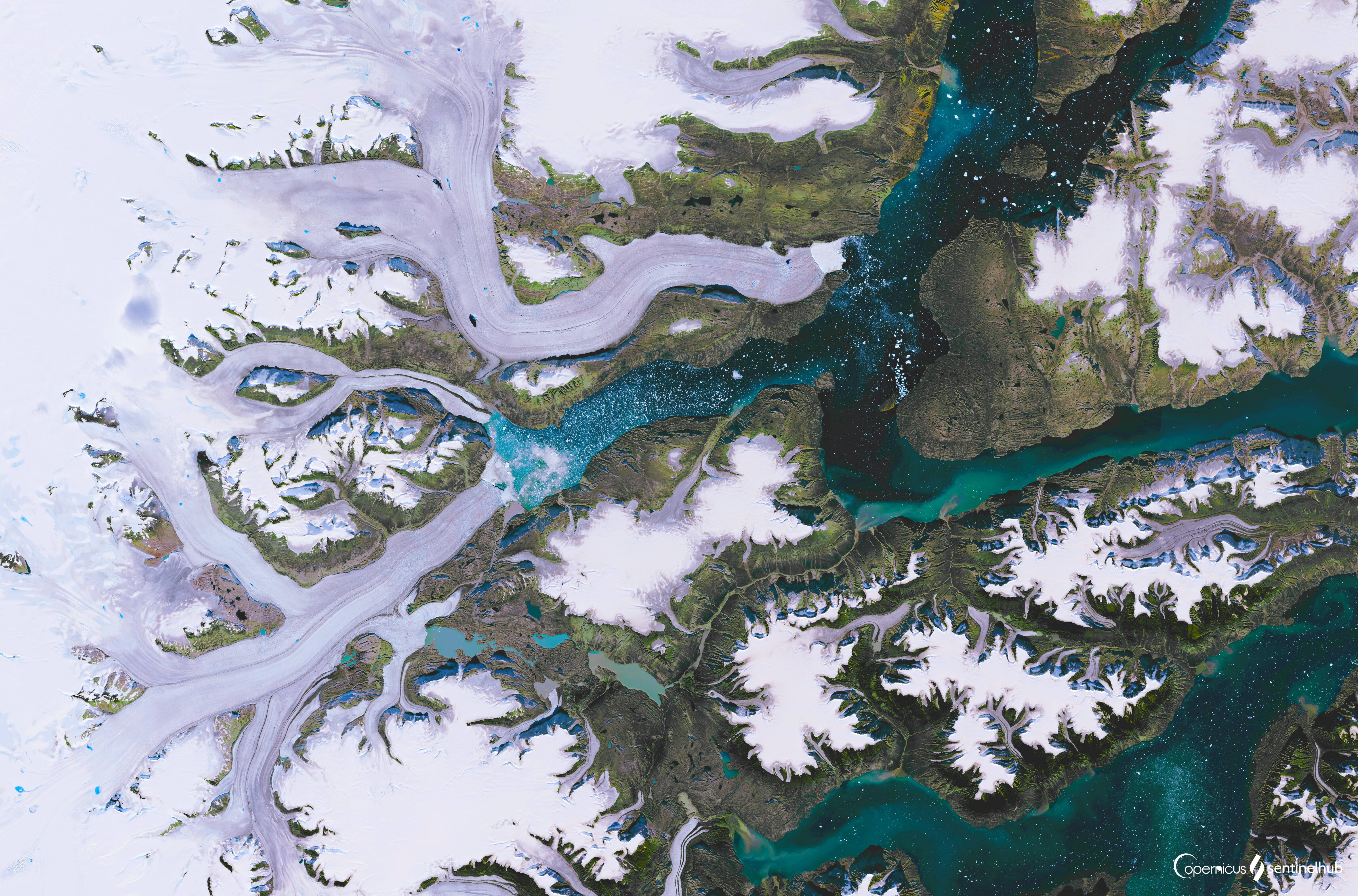 Greenland 桌布 壁紙 — 白雪覆蓋的山脈與蜿蜒的碧綠河流穿過崎嶇地形的鳥瞰圖。