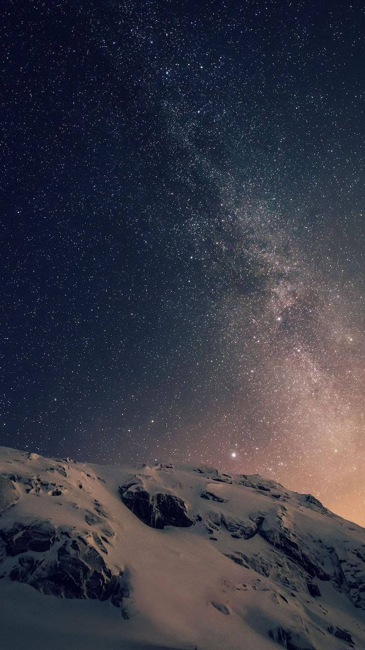 iPhone 桌布 壁紙 — 白雪覆蓋的山脊，在令人驚嘆的星空下，銀河散發著溫暖的色彩。