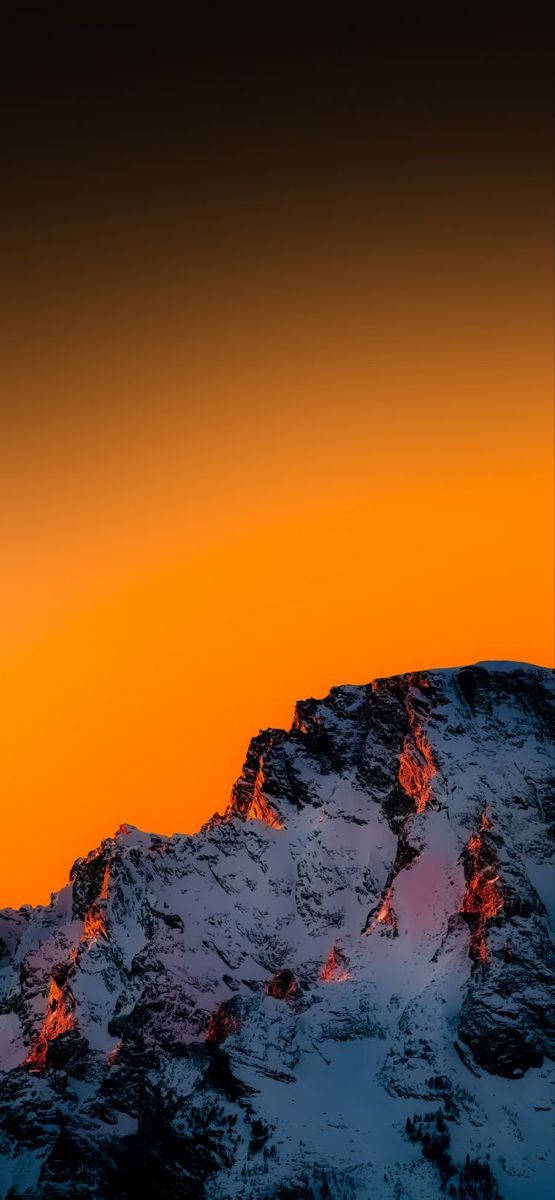 最佳智慧型手機 桌布 壁紙 — 白雪覆蓋的山脊沐浴在熾熱的橙色日落光芒中，映襯著漸變的天空。