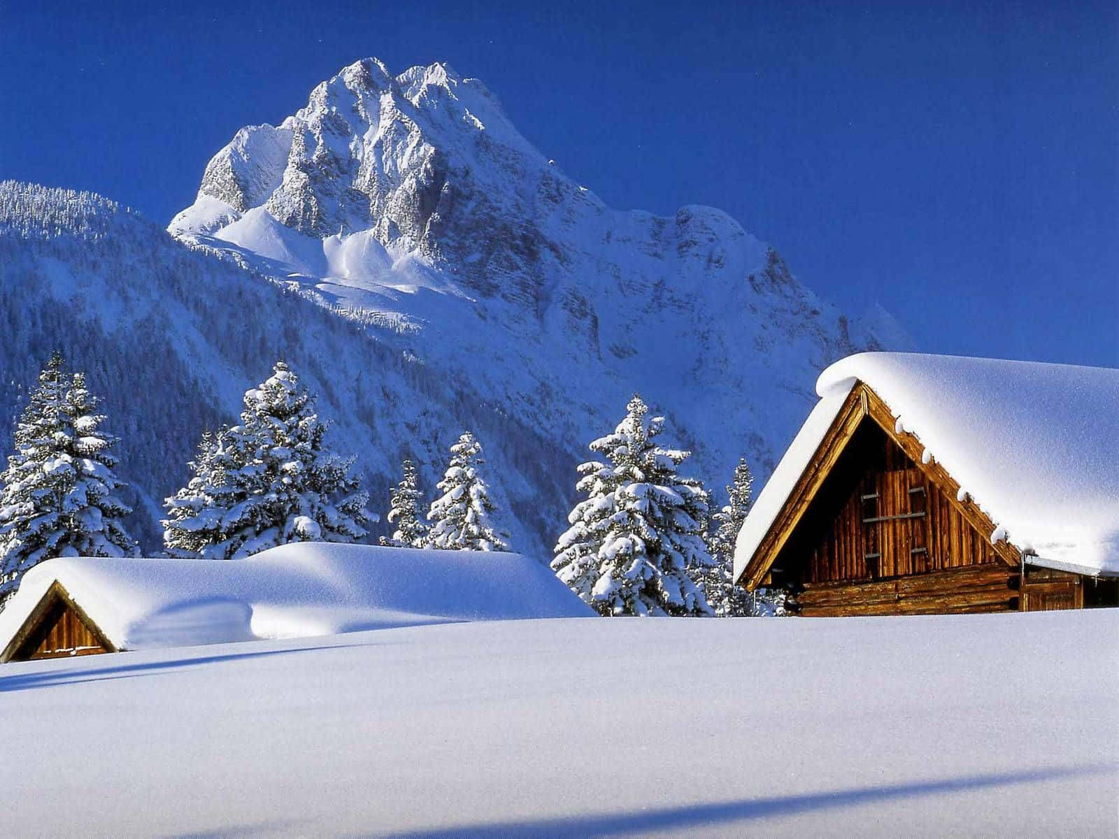 冬季桌面 桌布 壁紙 — 白雪覆蓋的木屋坐落在寧靜的冬季山谷中，天空湛藍清澈。