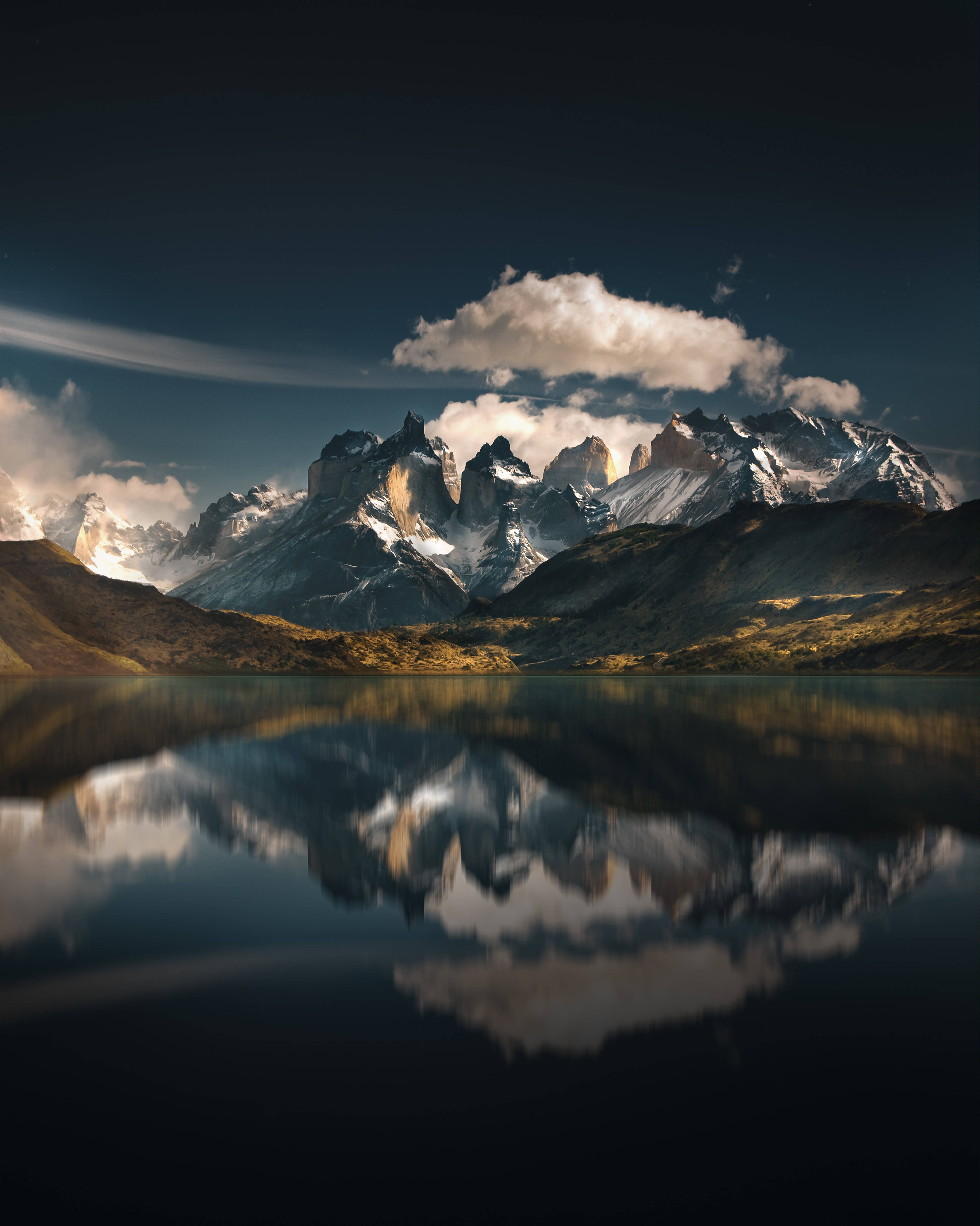 Chile 桌布 壁紙 — 白雪覆蓋的鋸齒狀山峰聳立在平靜的湖面上，在陰雲密布的暮色天空下映照出它們戲劇性的輪廓。