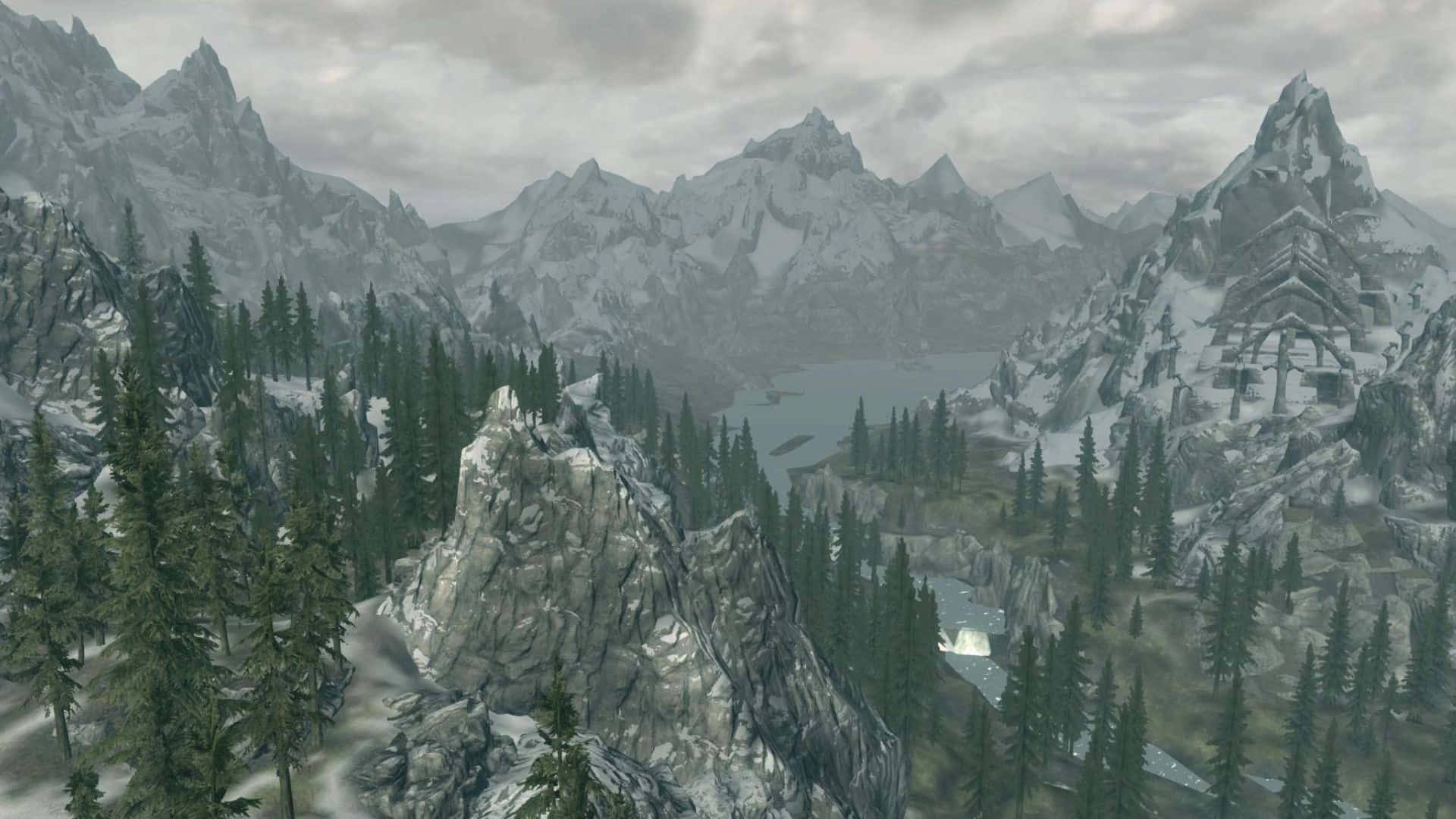 Skyrim Falkreath 桌布 壁紙 — 白雪覆蓋的鋸齒狀山脈聳立在霧氣瀰漫的湖泊之上，周圍是茂密的常綠森林，天空多雲。