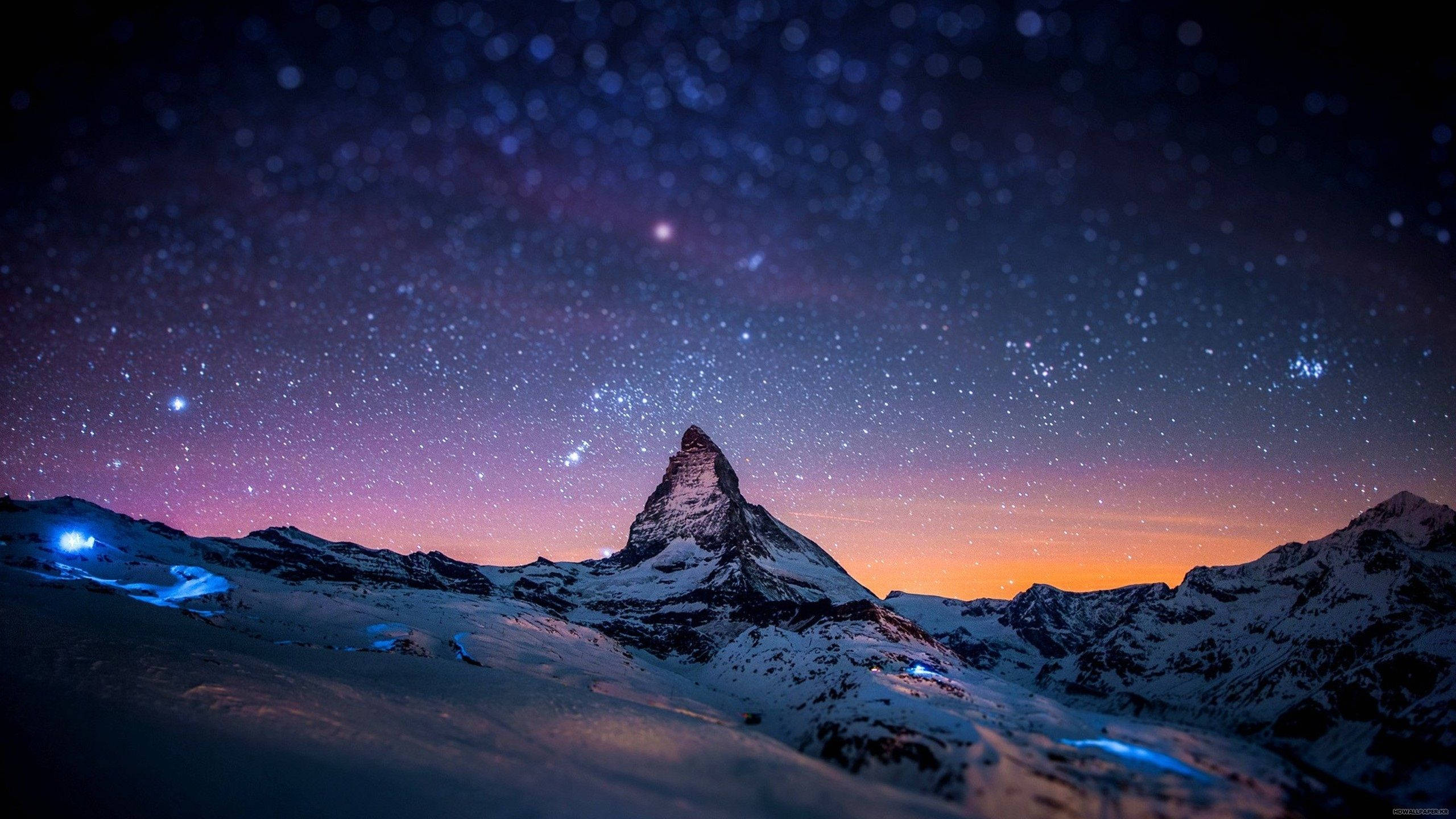 夜景城市風光等待您 壁紙 — 白雪覆蓋的馬特洪峰在星空暮色下聳立，帶有紫橙色漸變，下方有發光的藍色燈光。