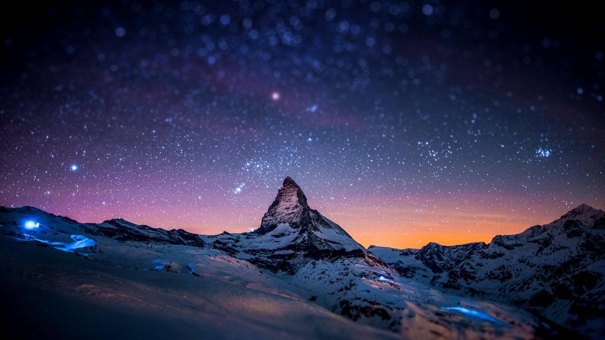 電腦 桌布 壁紙 — 白雪覆蓋的馬特洪峰在星空暮色下聳立，帶有紫橙色漸變和雪坡上發光的藍色燈光。