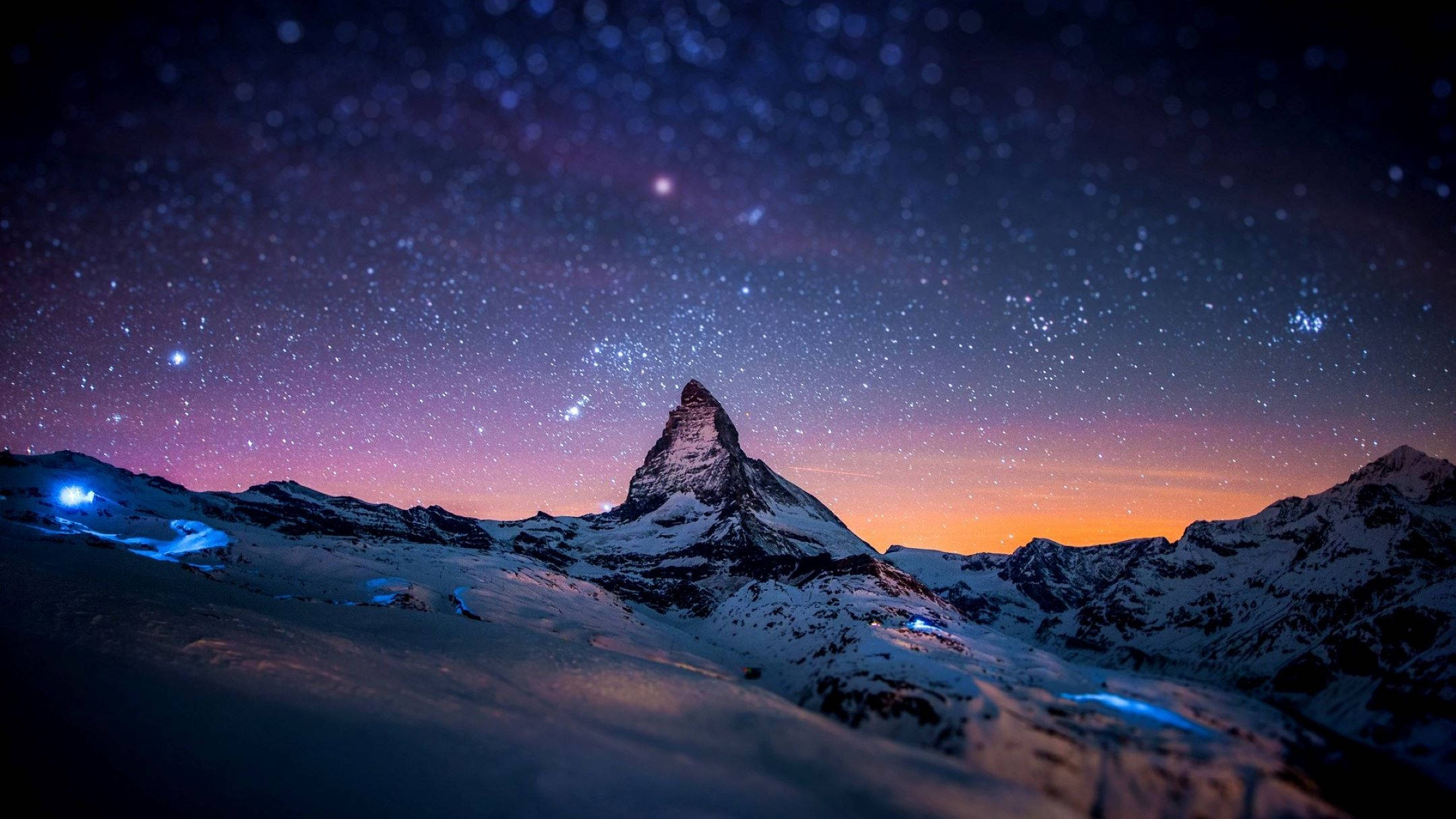 瑞士 桌布 壁紙 — 白雪覆蓋的馬特洪峰在星空暮色天空下呈現剪影，天空帶有紫橙色漸變，下方有發光的藍色燈光。