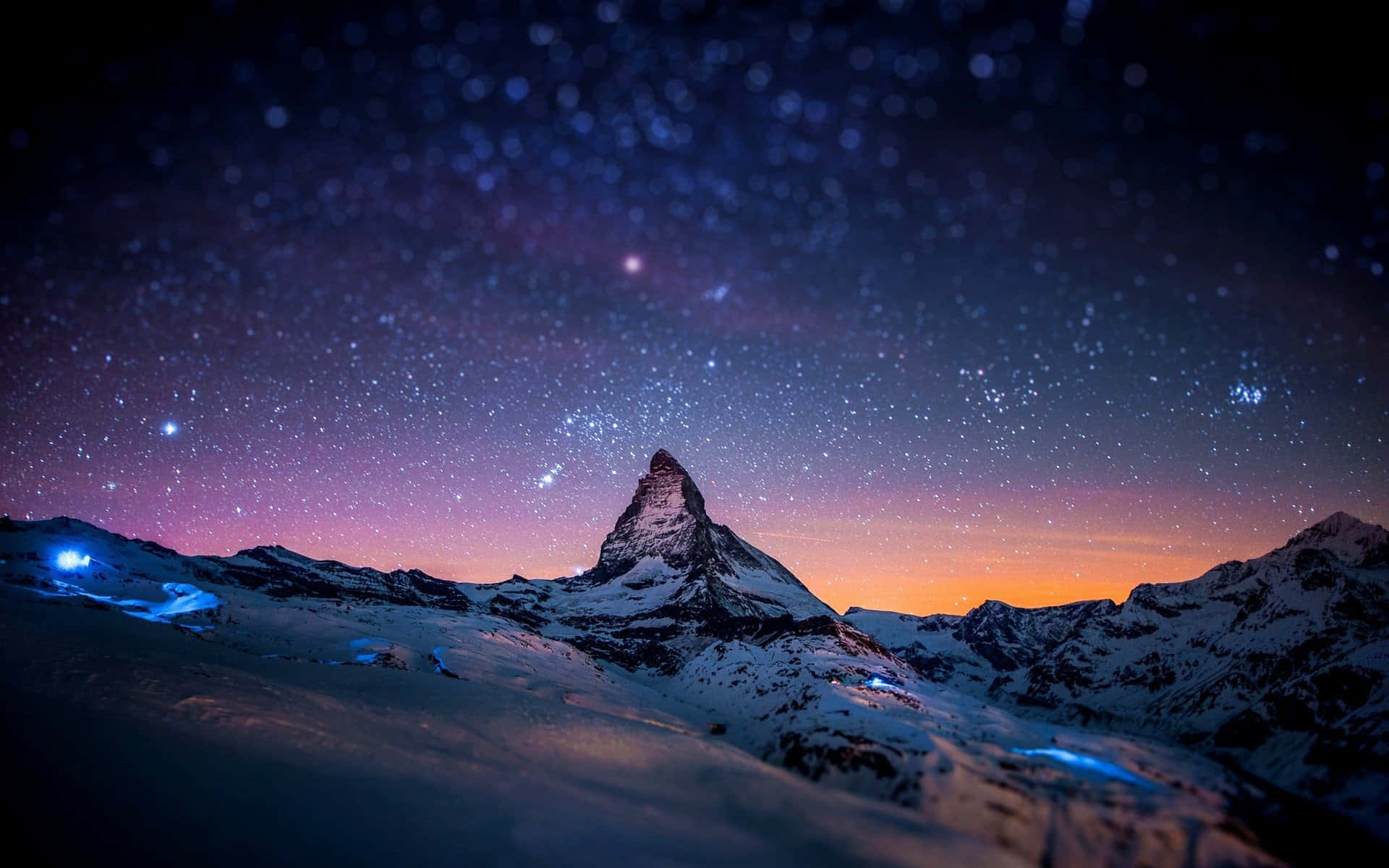 Stars 桌布 壁紙 — 白雪覆蓋的馬特洪峰在繁星點點的暮色天空下巍然聳立，雪坡上閃爍著藍色光芒。