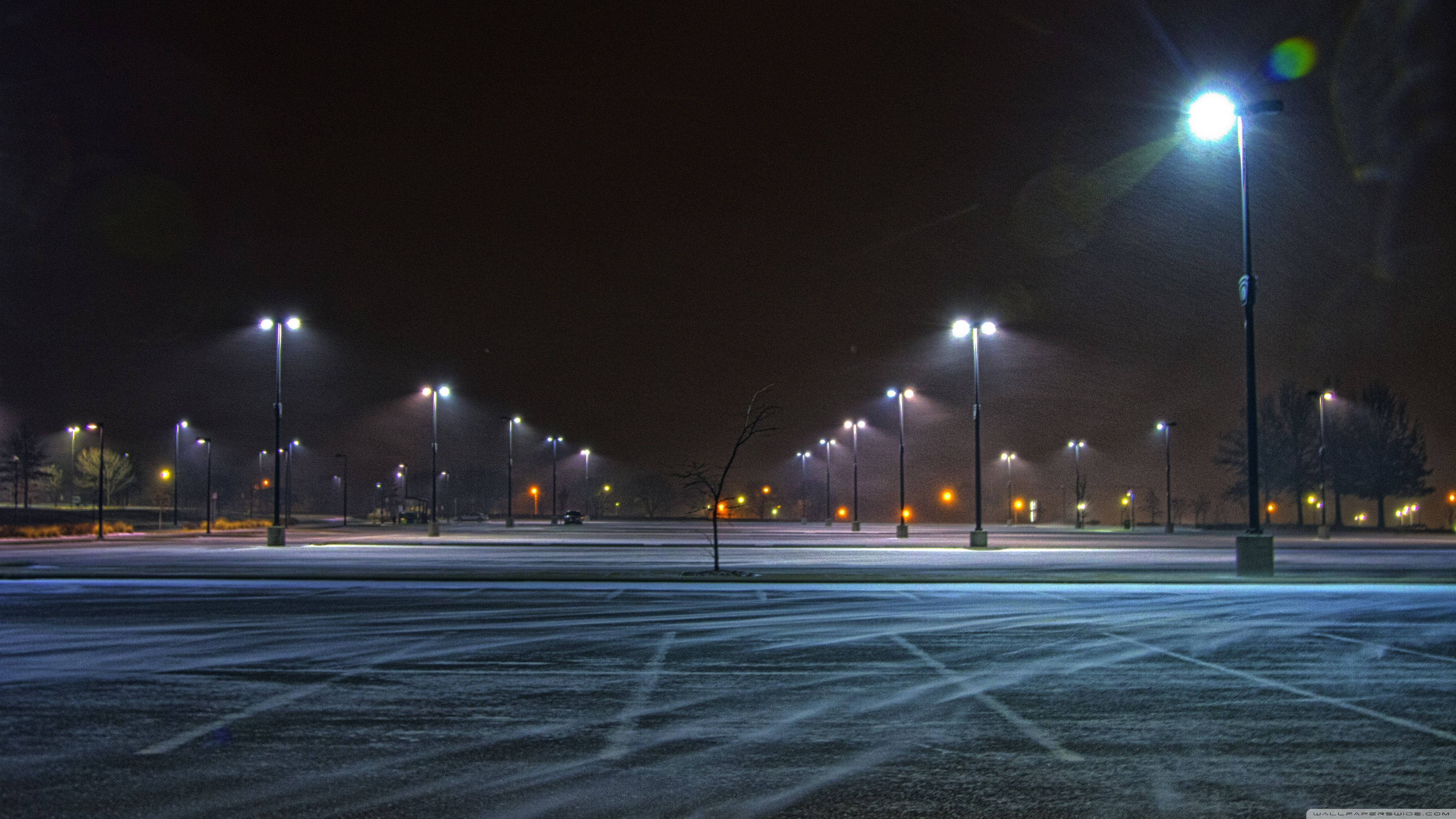 極高畫質 桌布 壁紙 — 白雪覆蓋空無一人的停車場，夜晚被一排排發光的街燈照亮，投下長長的影子。