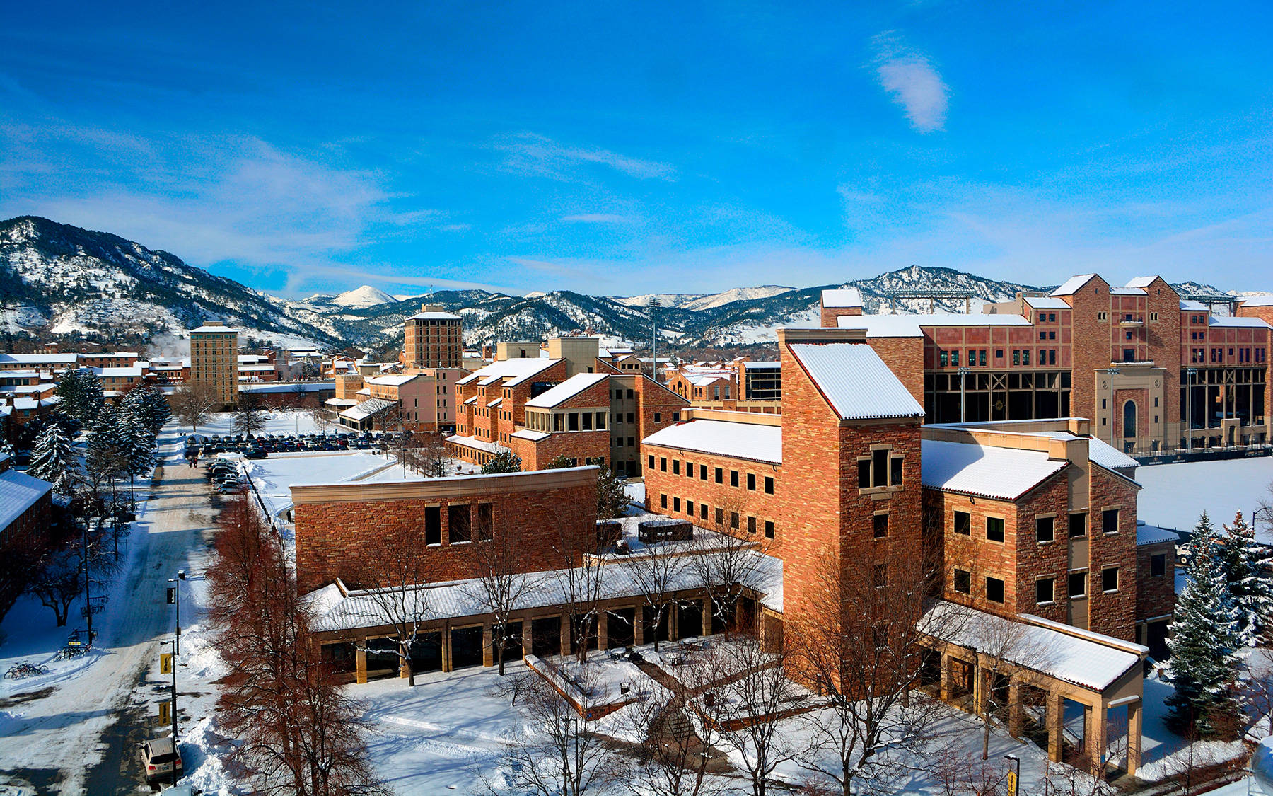 雪 桌布 壁紙 — 白雪覆蓋紅磚大學建築和光禿禿的樹木，在清澈的藍天下，遠處有積雪的山峰。