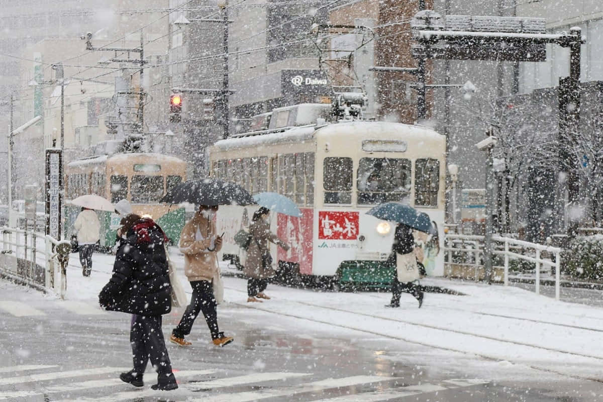 blizzard 桌布 壁紙 — 白雪覆蓋繁忙的日本街道，通勤者撐著傘在復古電車間穿梭，構成冬日城市景象。