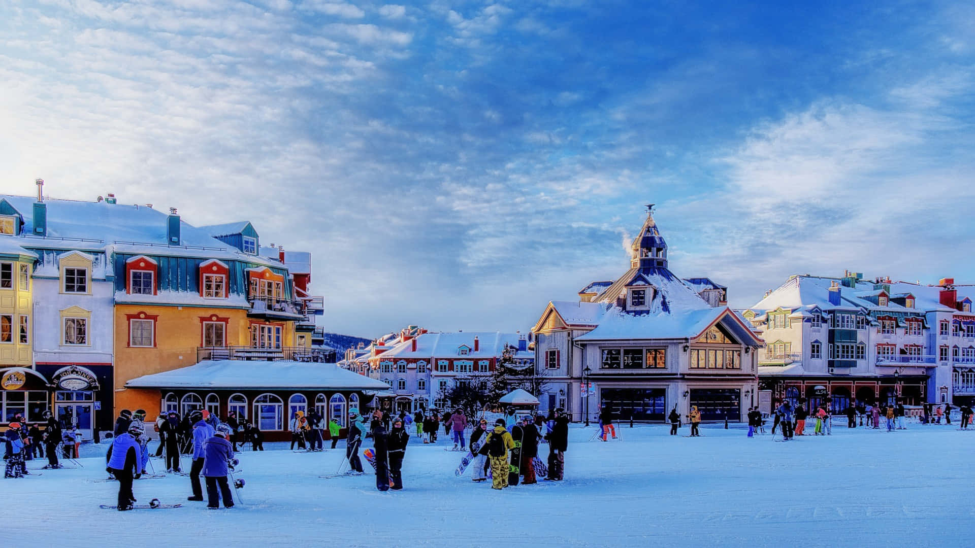 Ski Resort 桌布 壁紙 — 白雪覆蓋著一個充滿活力的歐洲城鎮廣場，人們在戲劇性的暮色天空下享受冬季運動。