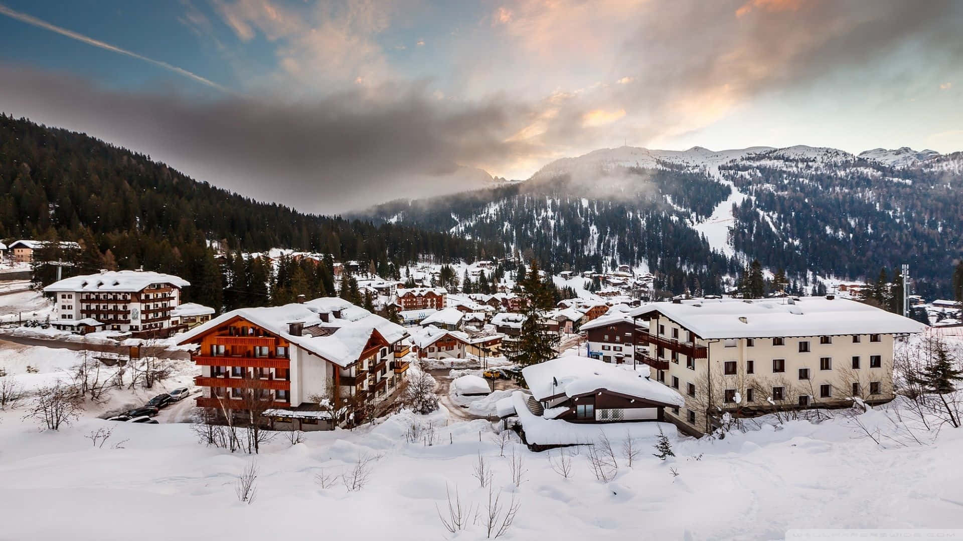 Snowy Village 桌布 壁紙 — 白雪覆蓋著一個坐落在群山之中、在戲劇性暮色天空下的舒適阿爾卑斯村莊。