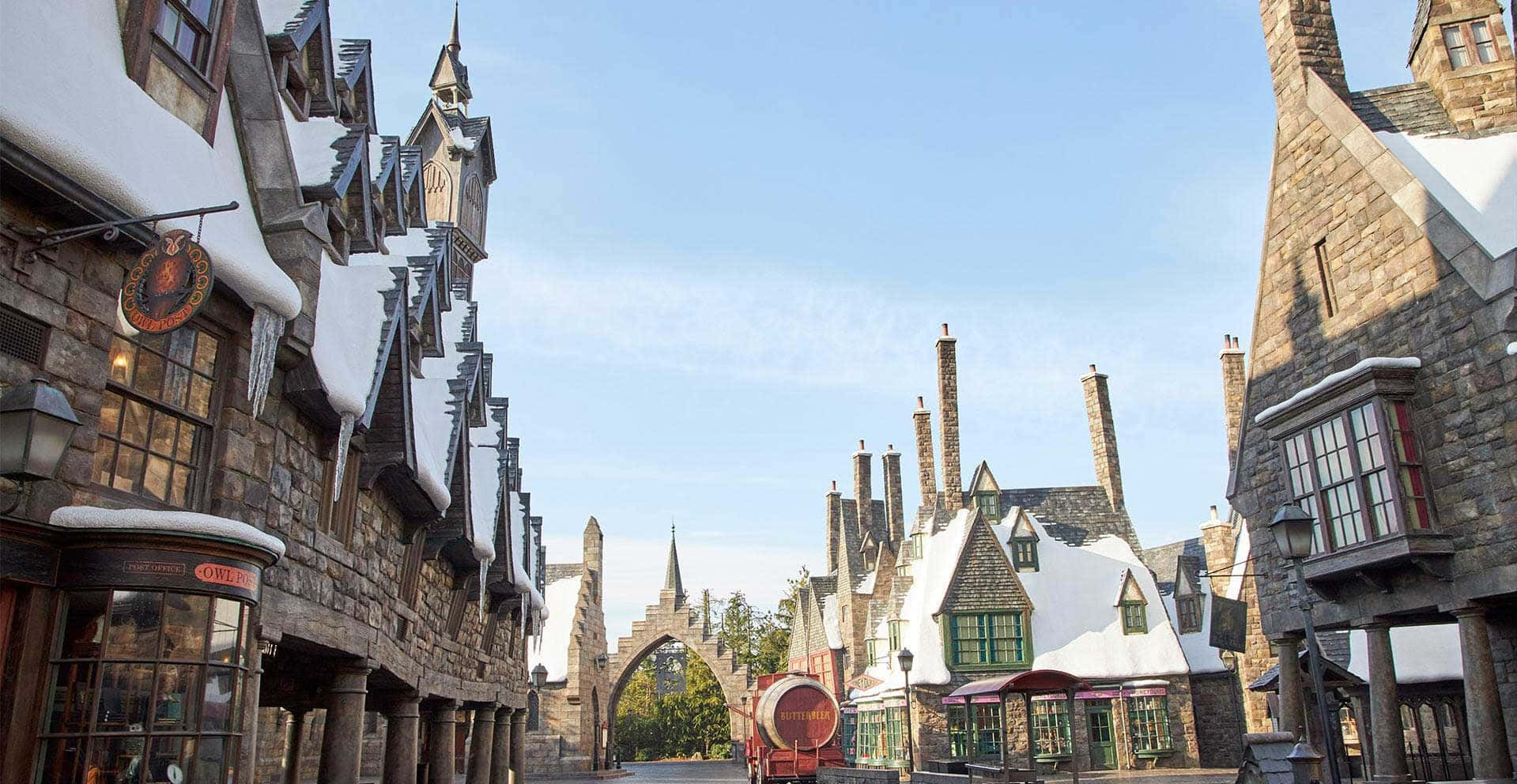 Hogsmeade 桌布 壁紙 — 白雪覆蓋著一個奇幻巫師村莊陡峭的屋頂和石頭建築，天空清澈湛藍。