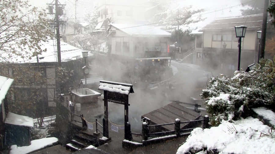 High Resolution Snow 桌布 壁紙 — 白雪覆蓋著一個寧靜的日本溫泉村莊，蒸氣從被傳統木建築環繞的溫泉池中升起。