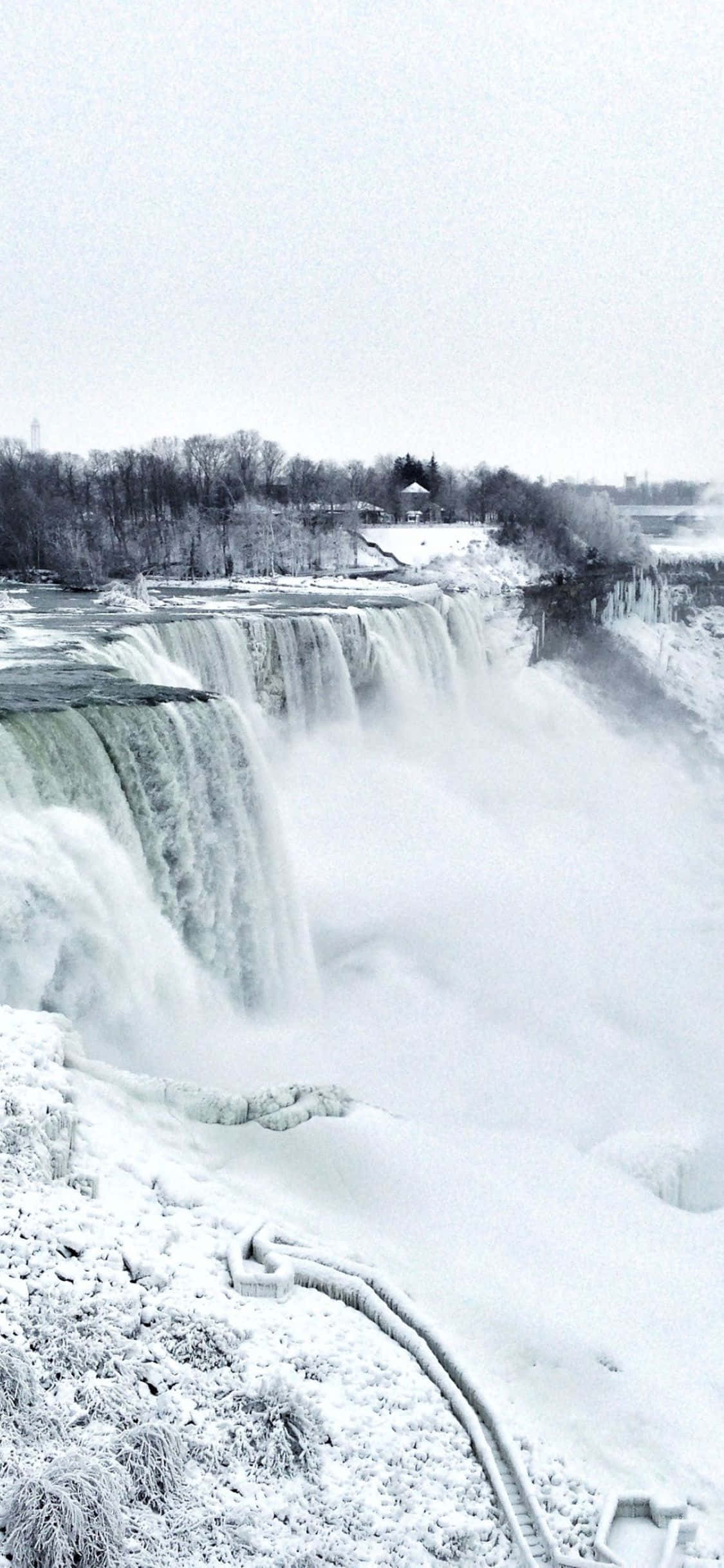 Niagara Falls 桌布 壁紙 — 白雪覆蓋著一個巨大瀑布的冰凍邊緣，在陰天之下穿過冬日景觀傾瀉而下。