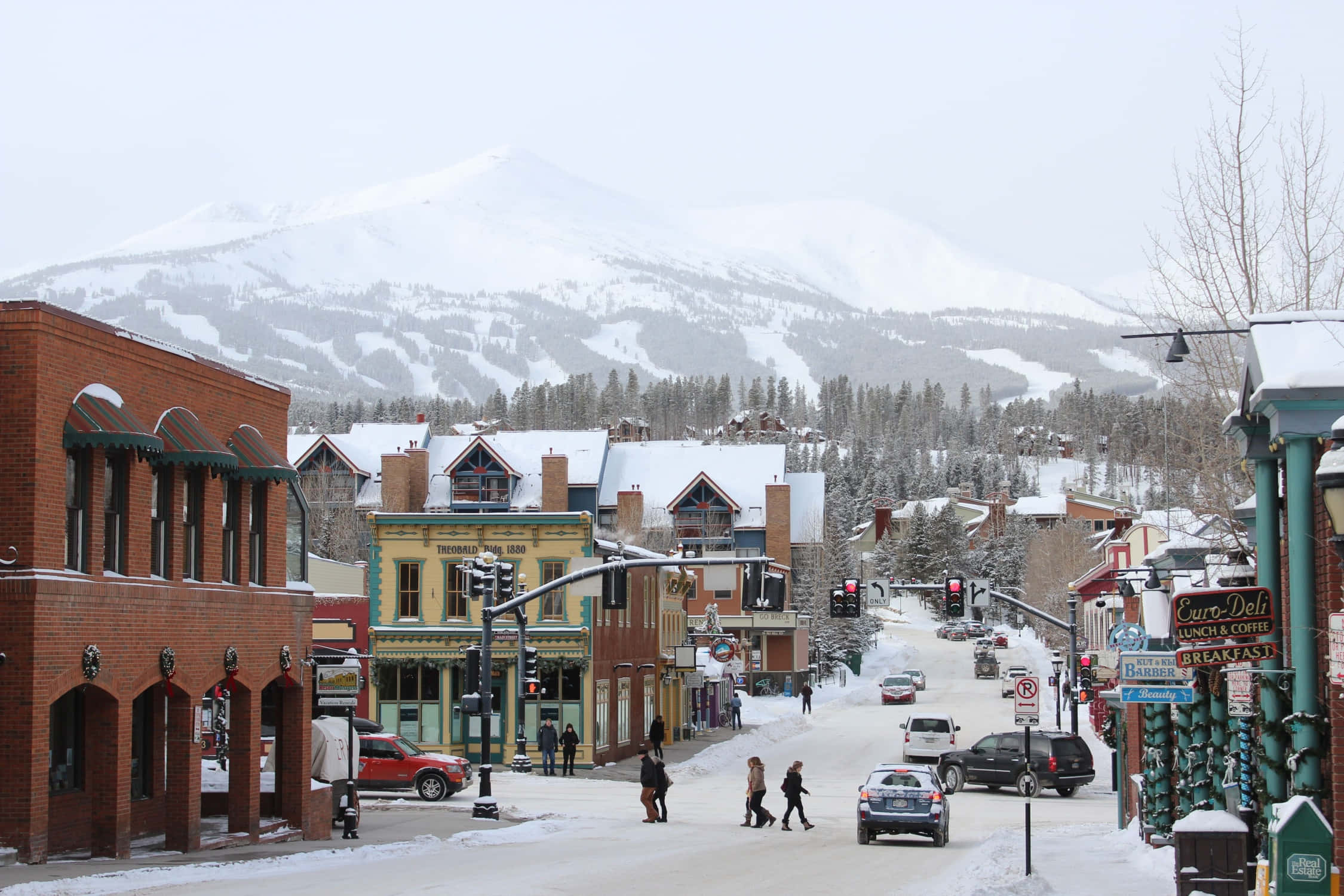 Colorado 桌布 壁紙 — 白雪覆蓋著一條古雅的山城街道，兩旁是歷史悠久的磚造建築，遠方是白雪覆蓋的山峰，天空灰濛濛。